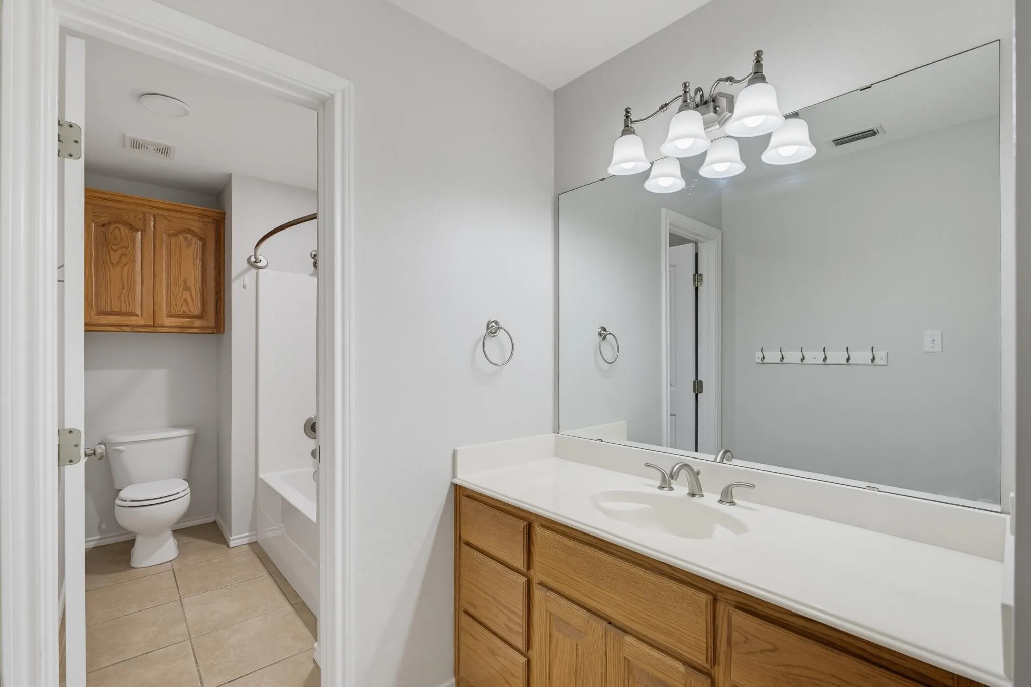 Spa-inspired primary bathroom featuring a wood-finish vanity with dual sinks, white quartz countertop, and an expansive framed mirror