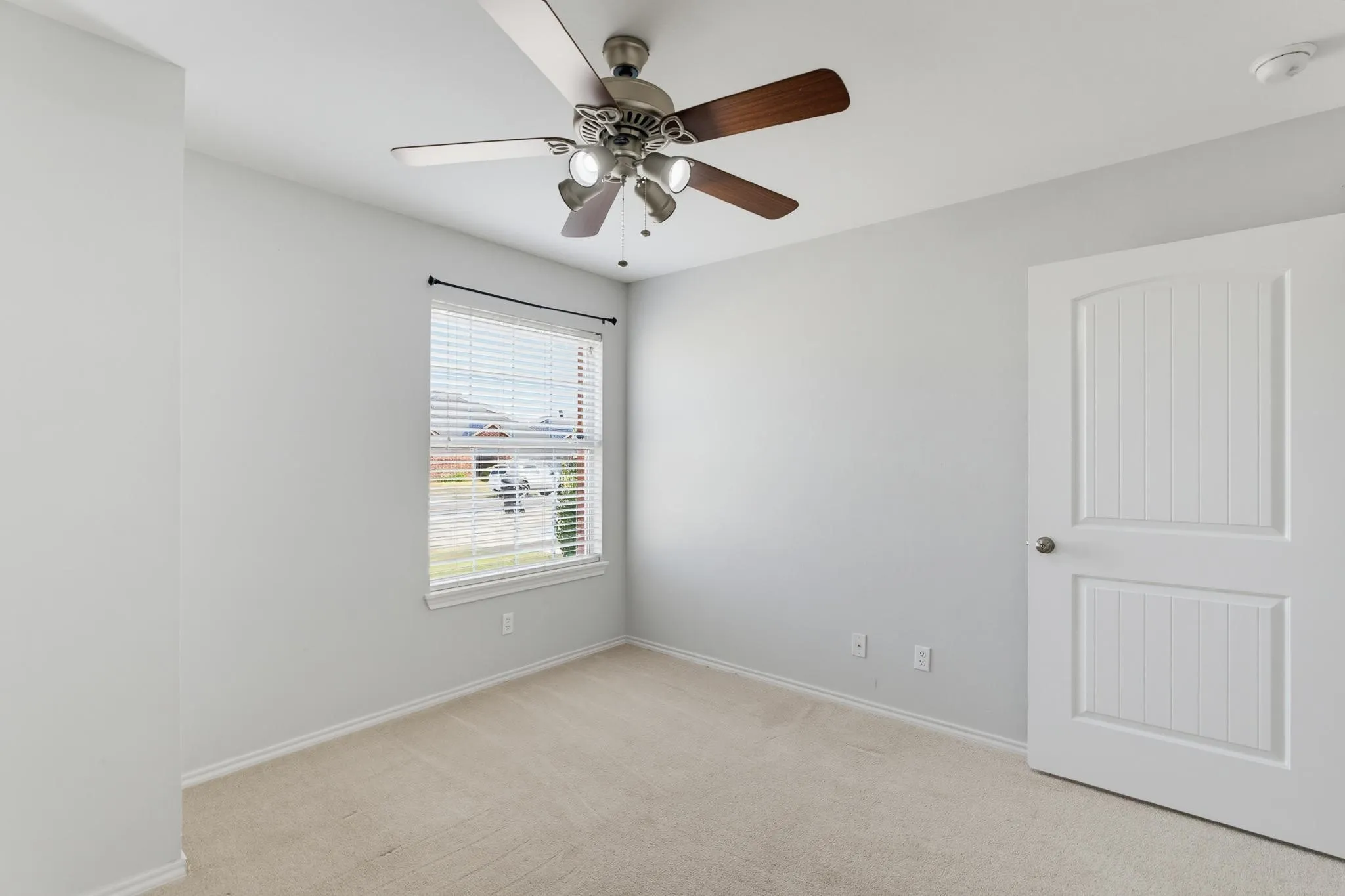 Bright bedroom featuring neutral carpeting, a ceiling fan with integrated lighting, large window with horizontal blinds, and a six-panel closet door