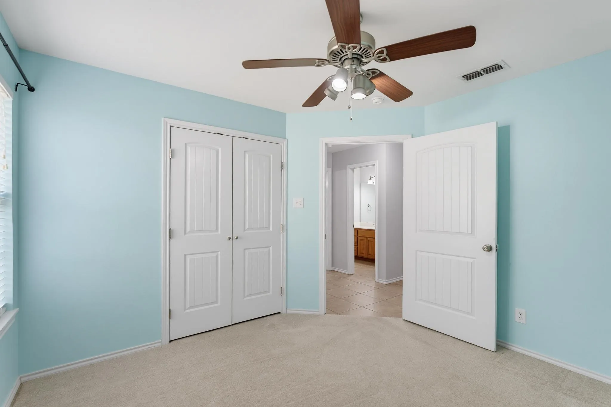 Spacious bedroom with soft blue walls, neutral carpeting, and ceiling fan with integrated lighting