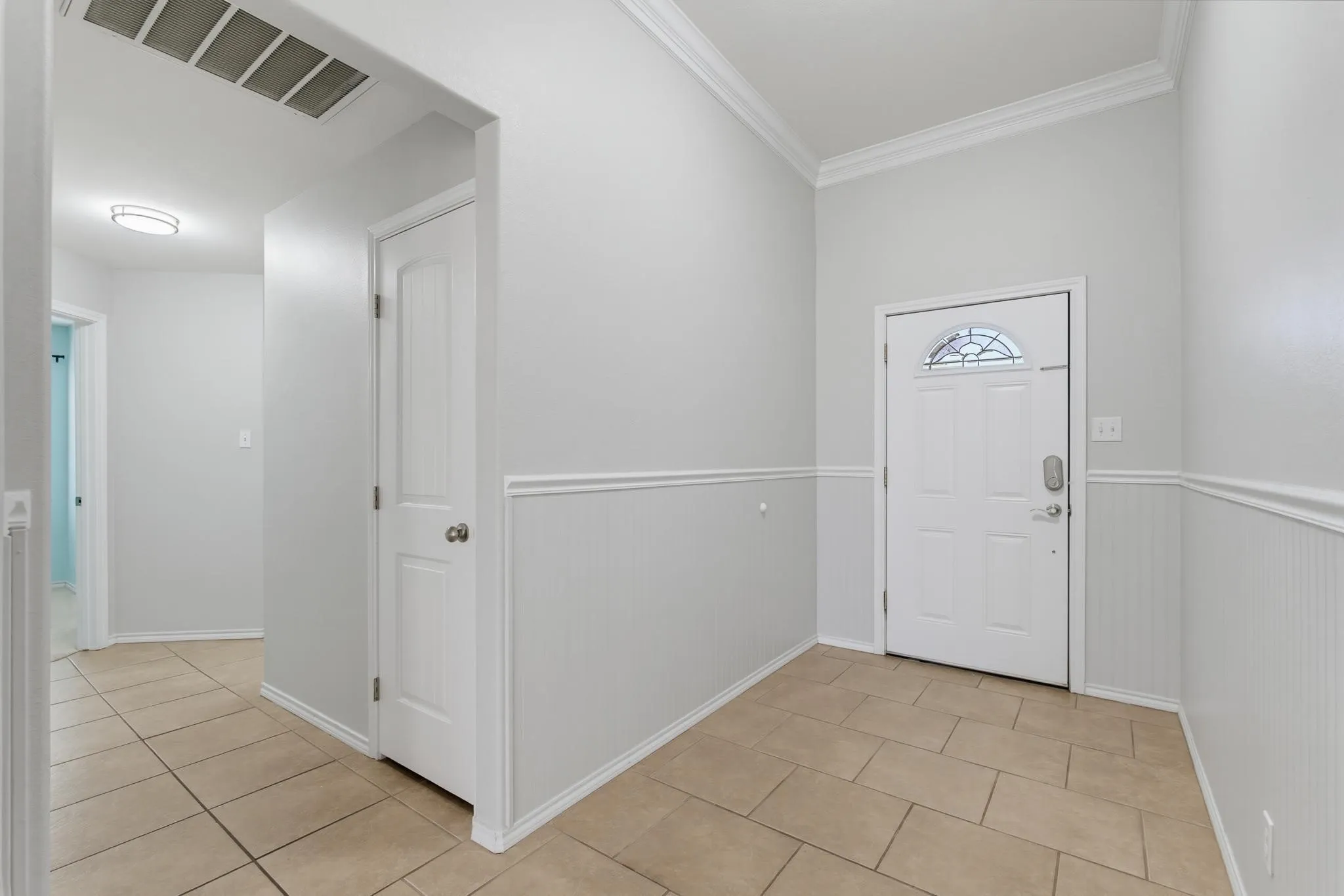 Bright, open foyer featuring tile flooring, white wainscoting with chair rail detailing, and dual white six-panel doors with transom windows