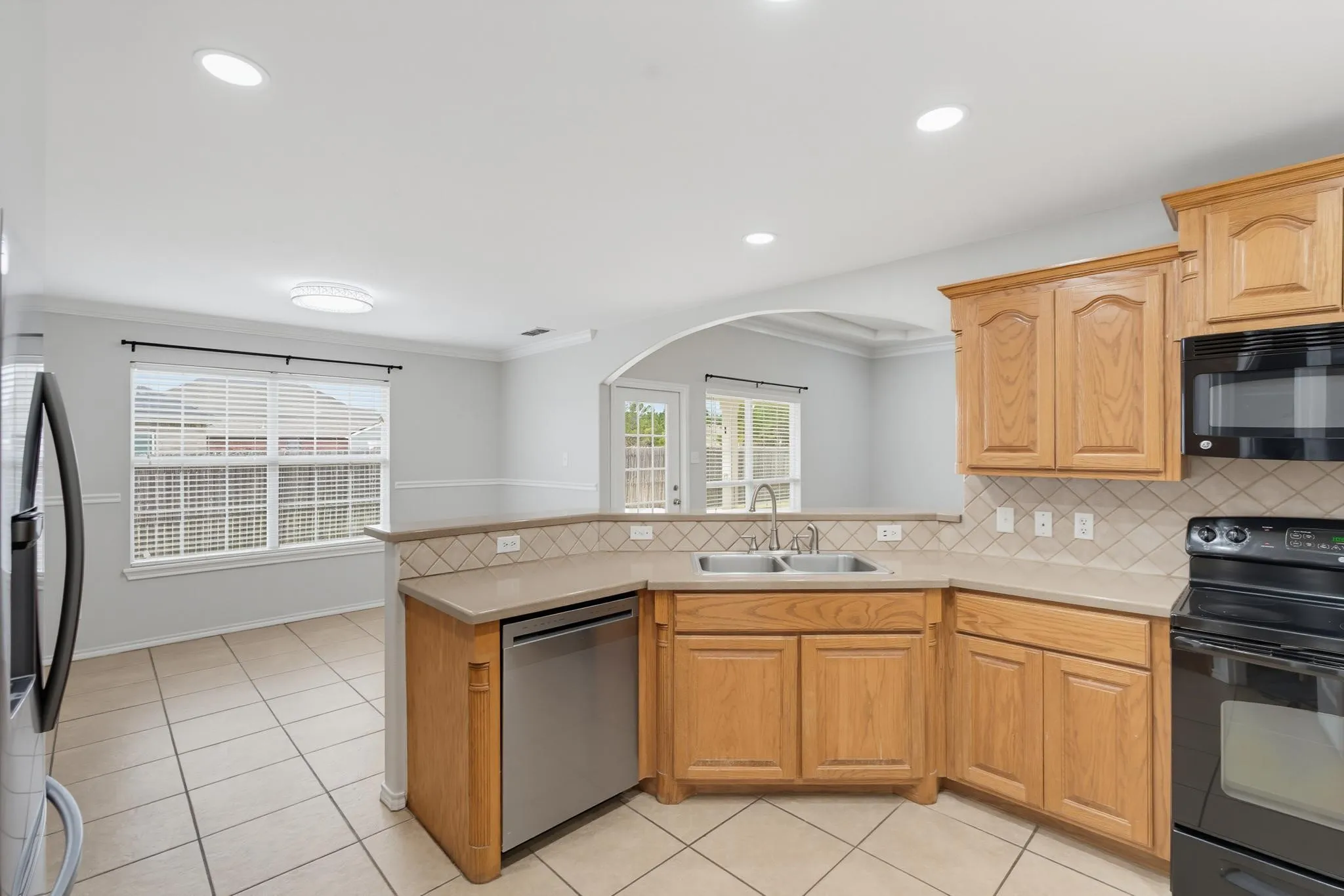 Spacious kitchen featuring warm wood cabinetry, stainless steel appliances, tile countertops, a center island with seating, and recessed lighting throughout