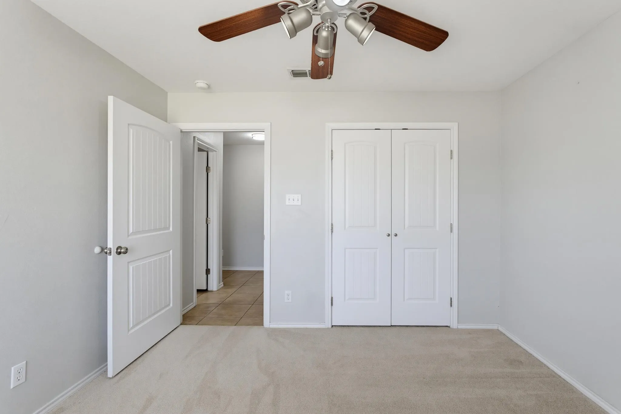 Spacious bedroom featuring neutral carpeting, ceiling fan with integrated lighting, and dual closet doors providing ample storage