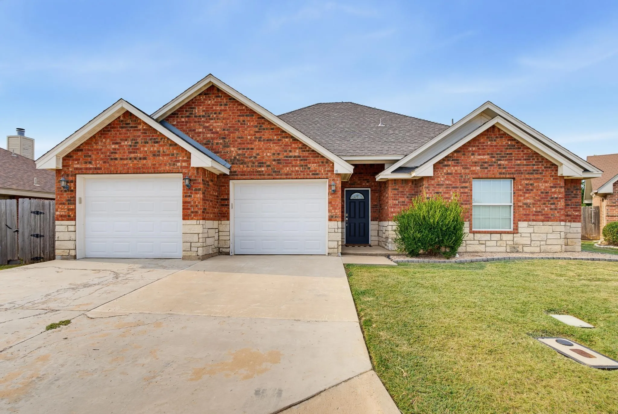 Brick and stone exterior with dual two-car garage doors, pitched roofline with multiple gables, and manicured front lawn with established landscaping