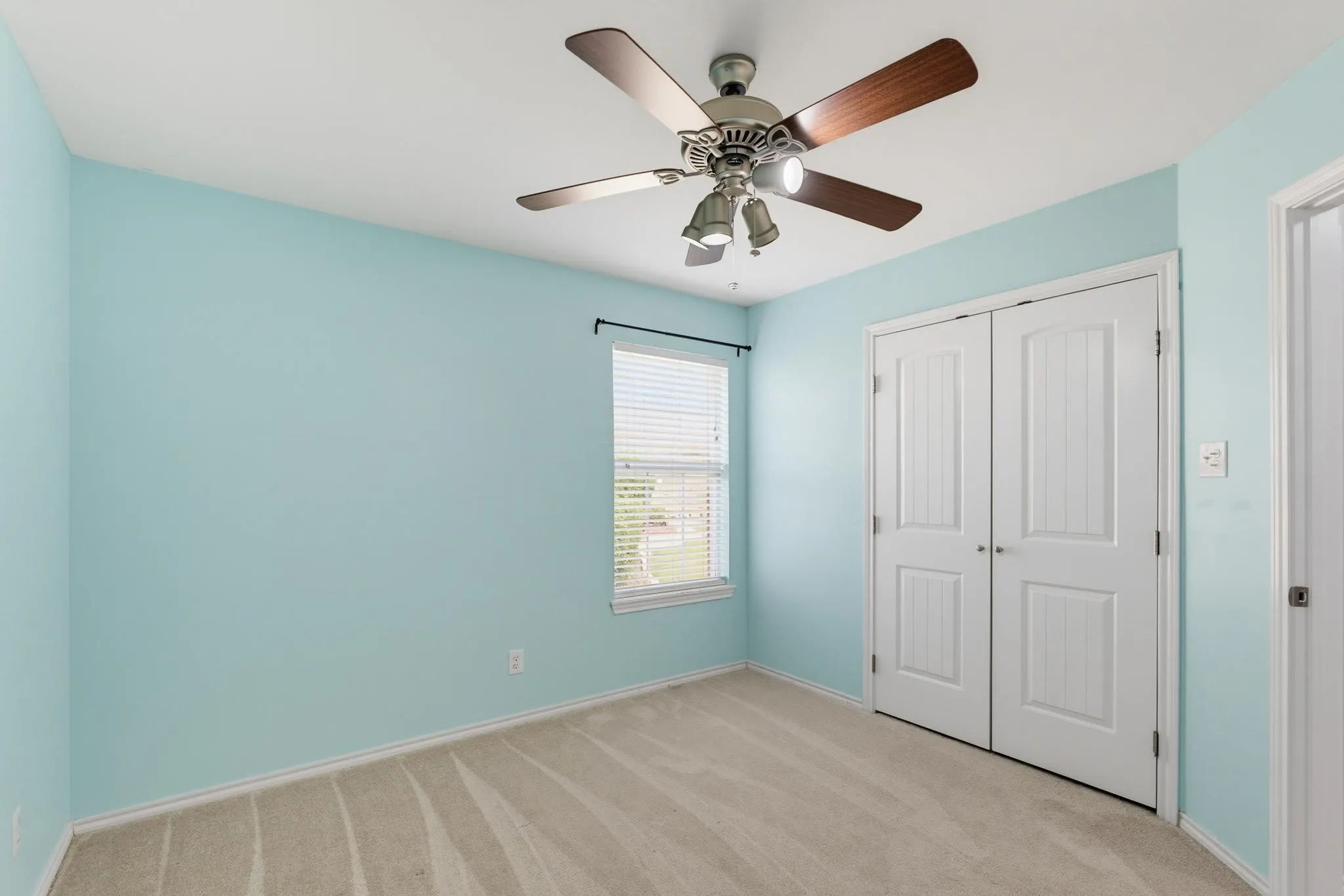 Bright bedroom featuring soft turquoise walls, laminate wood-finish flooring, and a ceiling fan with integrated lighting