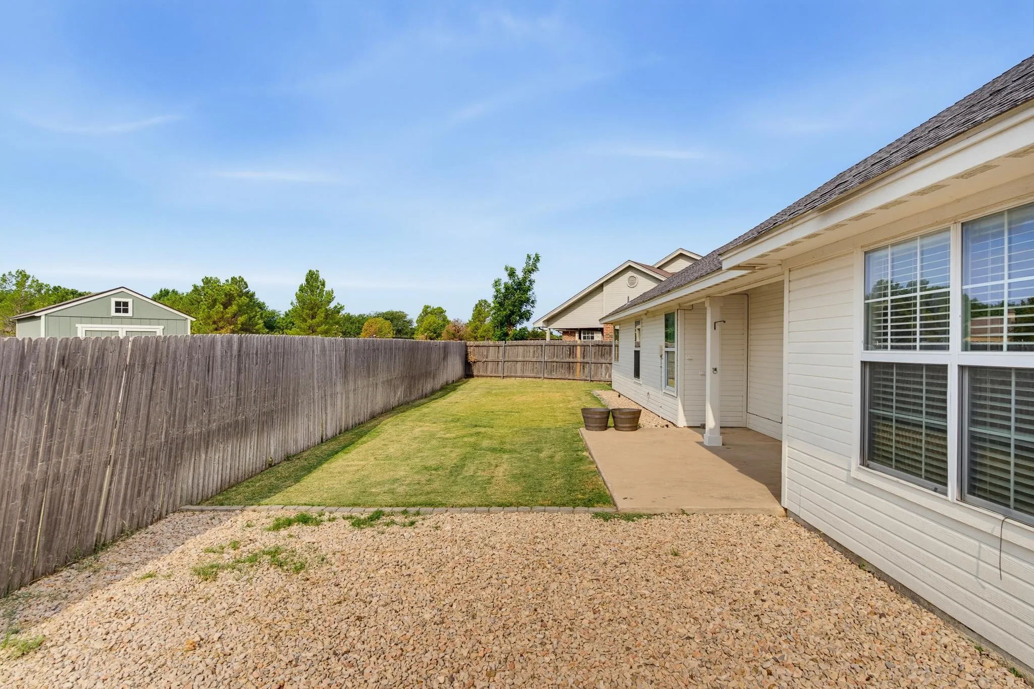 Expansive backyard featuring a manicured lawn, mature landscaping, and wooden privacy fencing