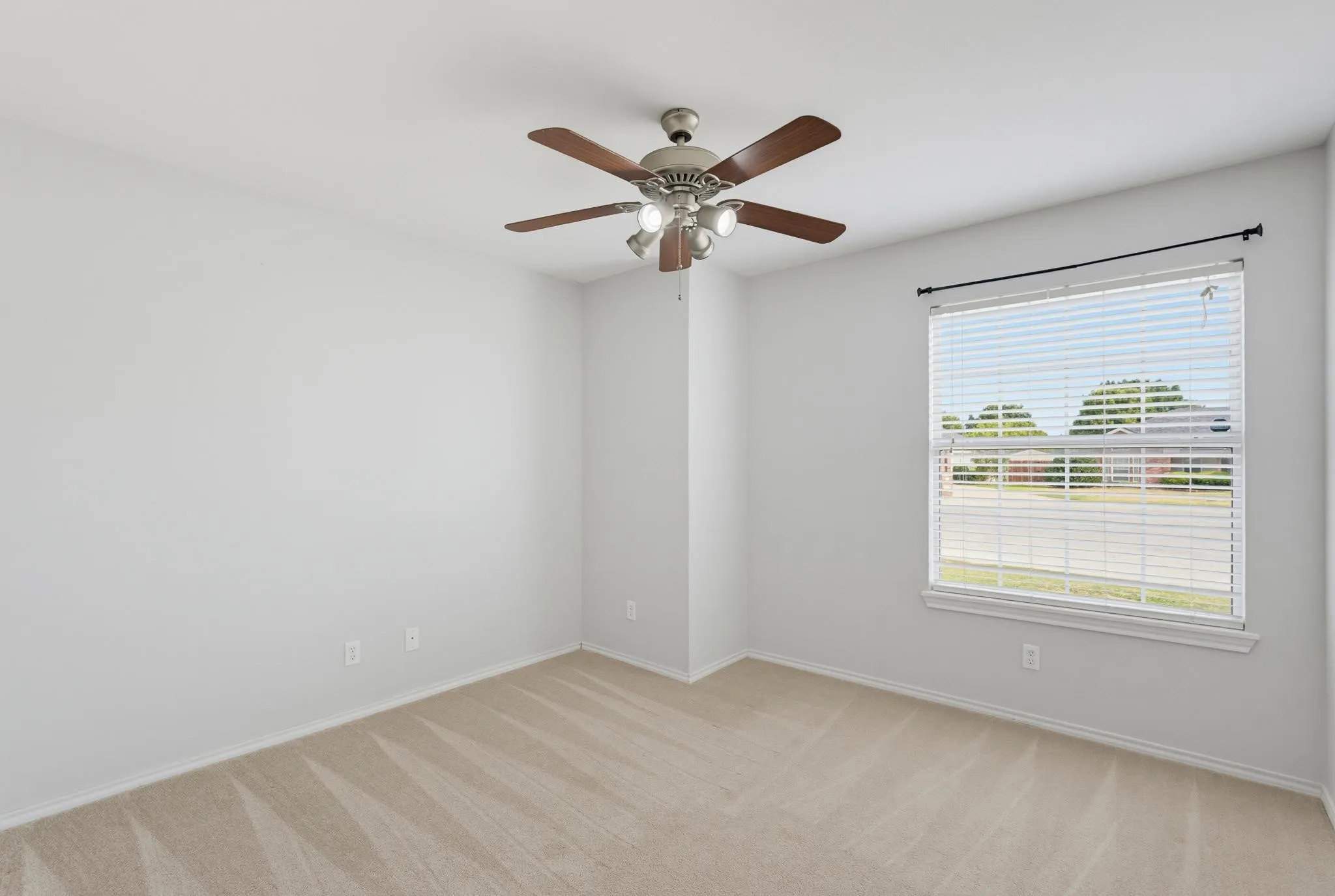 Bright corner bedroom with wood-finish flooring, ceiling fan with integrated lighting, and dual windows with horizontal blinds providing natural light and ventilation options