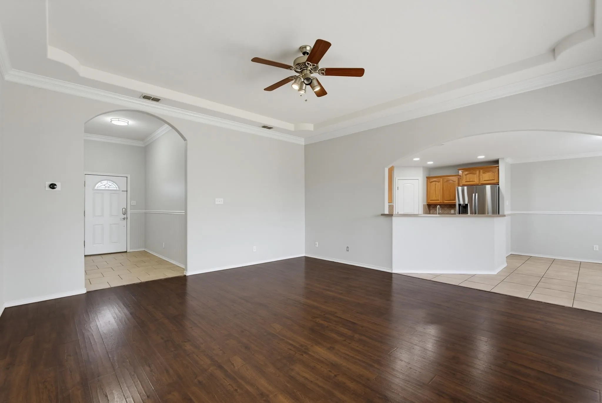 Tray ceiling with crown molding, wood-finish flooring, ceiling fan, arched doorways, and a breakfast bar