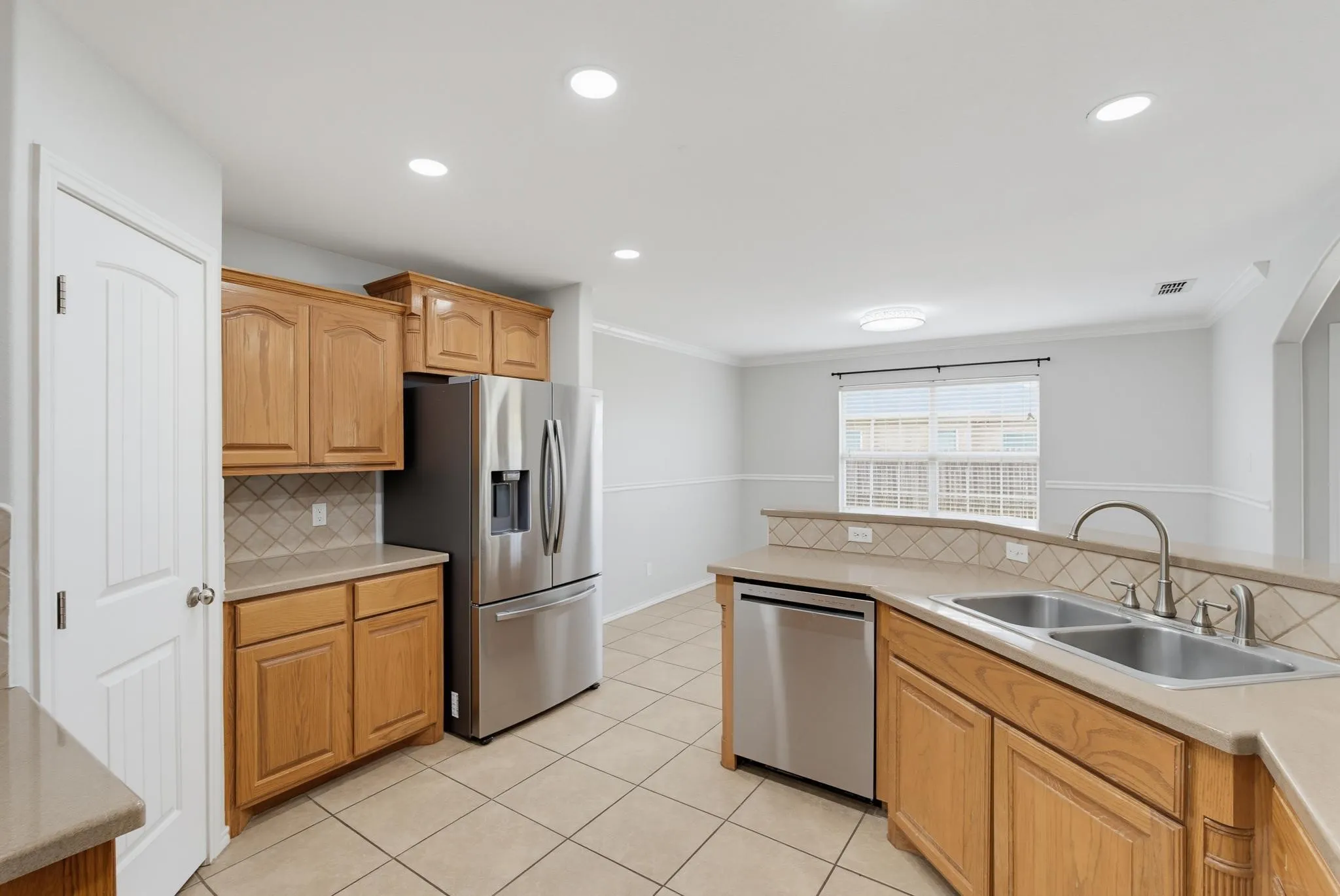 Kitchen featuring wood cabinetry, stainless steel appliances, dual basin sink, tile flooring, and a tiled backsplash