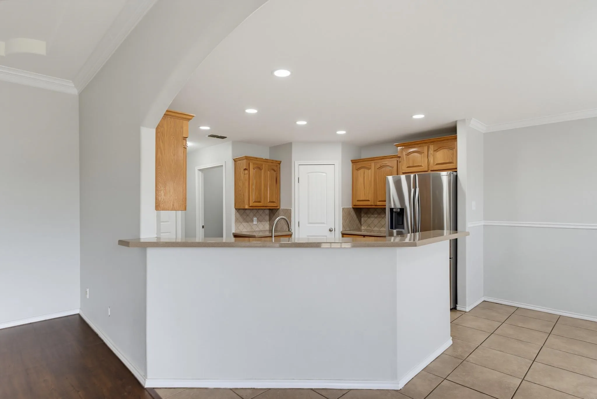 Kitchen with wood cabinetry, stainless steel refrigerator, tile backsplash, and recessed lighting
