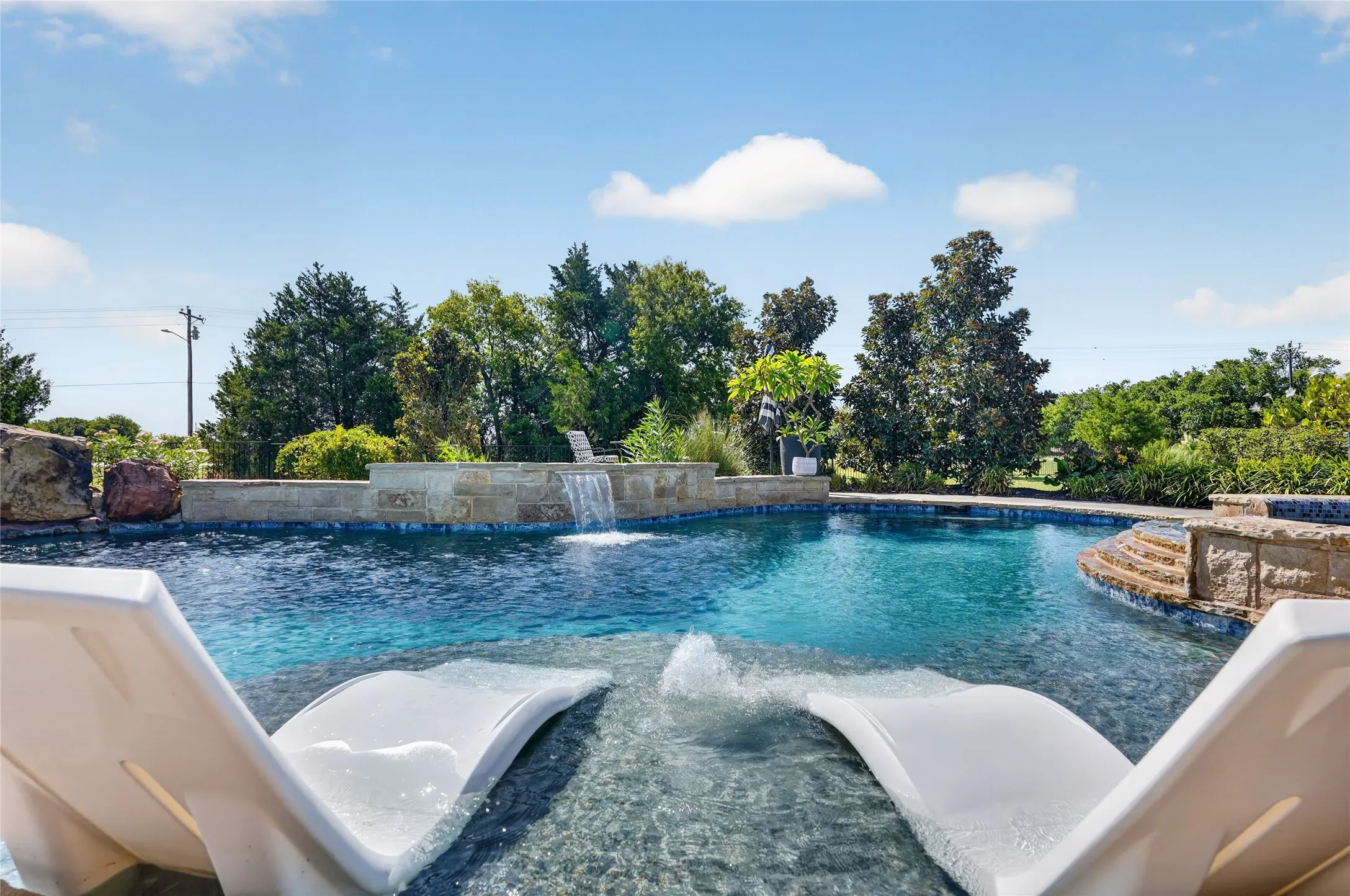Private backyard oasis featuring a built-in pool with a waterfall, stone-faced spa, and integrated sun shelf