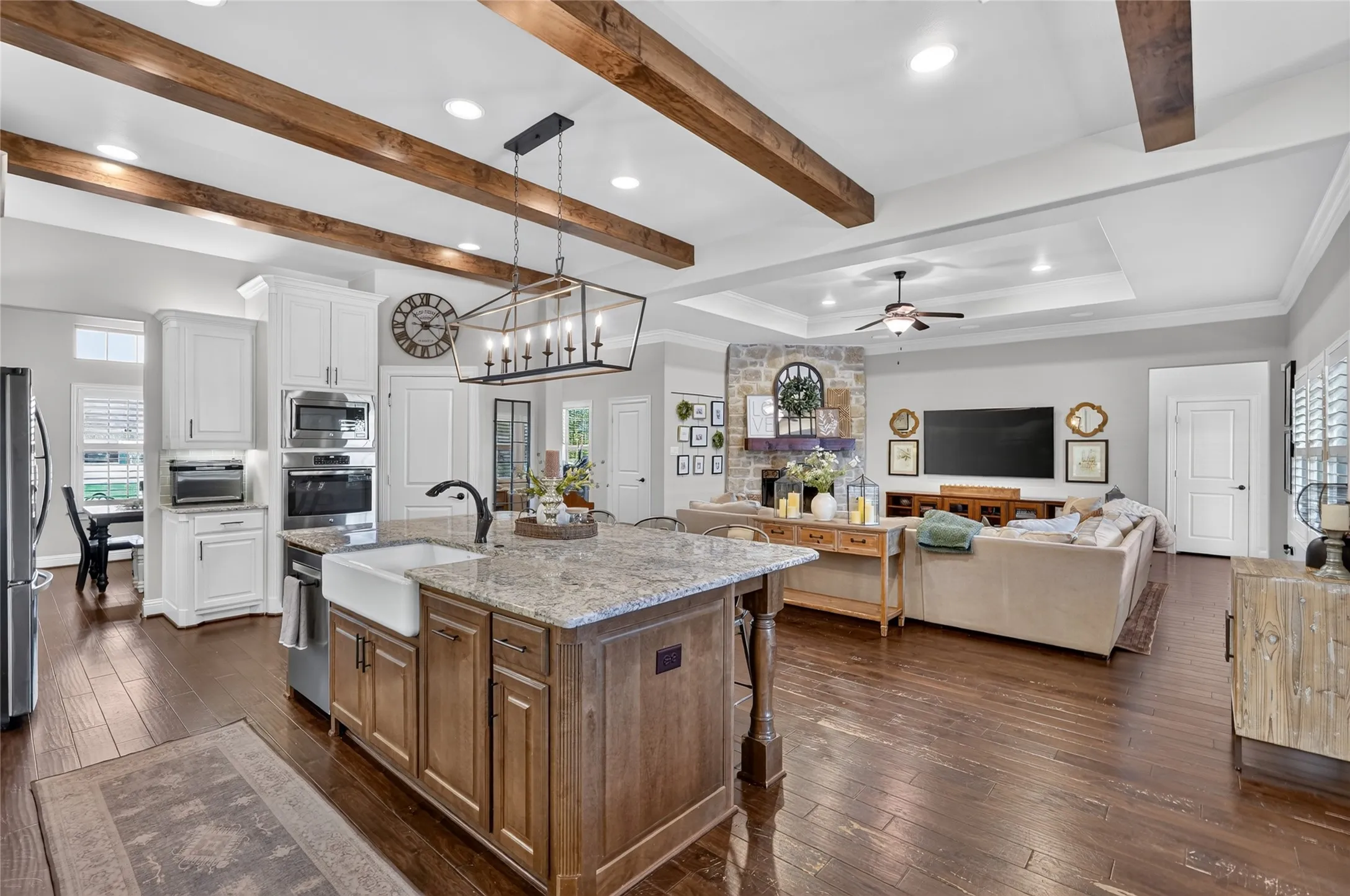 Open-concept kitchen and living area featuring exposed timber ceiling beams, recessed lighting, and a large island with granite countertop and wood cabinetry