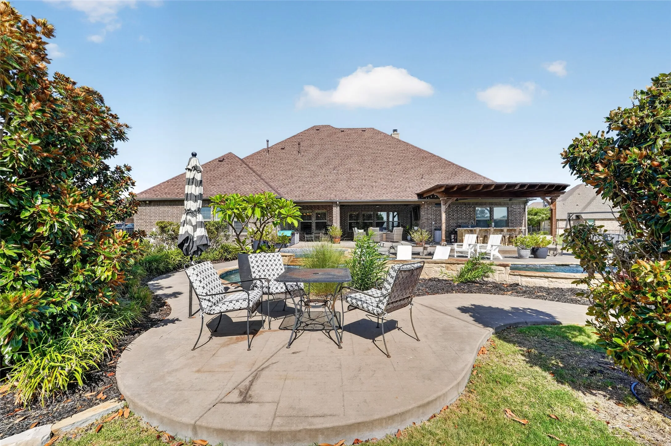 Expansive backyard featuring a large patio, built-in outdoor kitchen with pergola, swimming pool, and mature landscaping