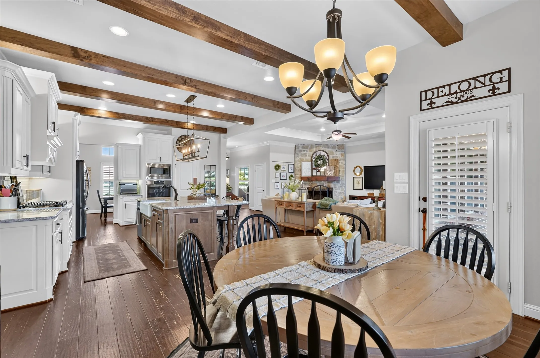 Open-concept kitchen and dining area featuring exposed wood beam ceiling details, pendant lighting, wood-finish flooring throughout, and a round dining table with seating for multiple guests