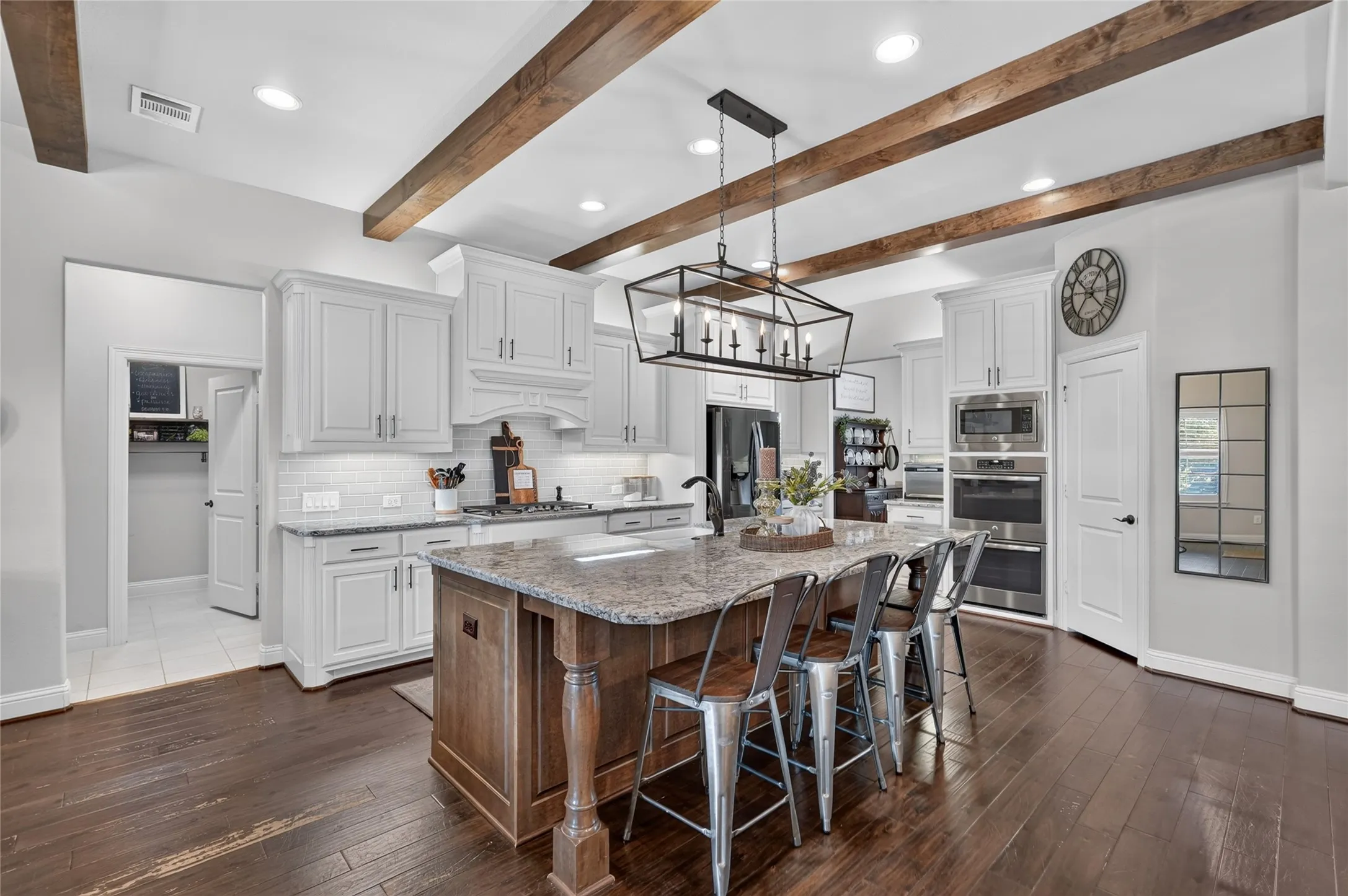 Chef's kitchen featuring white cabinetry, stainless steel appliances, and a large wood-finish island with stone countertops and seating for multiple guests