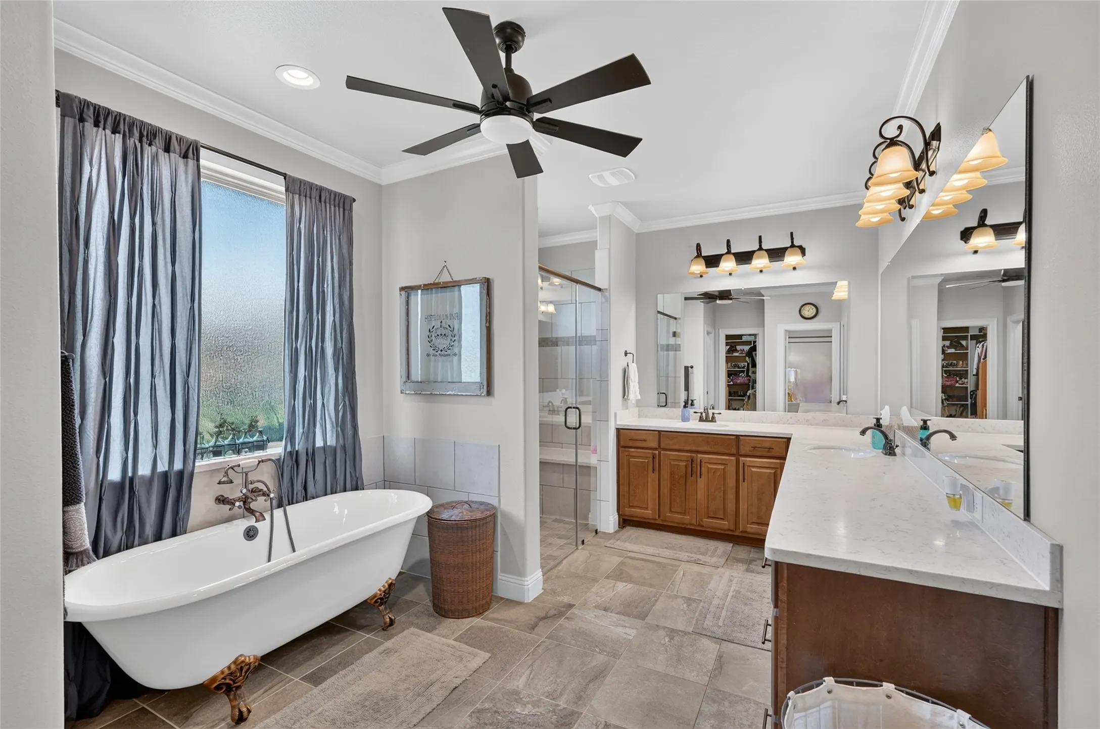Freestanding clawfoot tub with an antique-finish faucet, dual vanity with undermount sinks and light countertops, glass-enclosed shower, and tile flooring