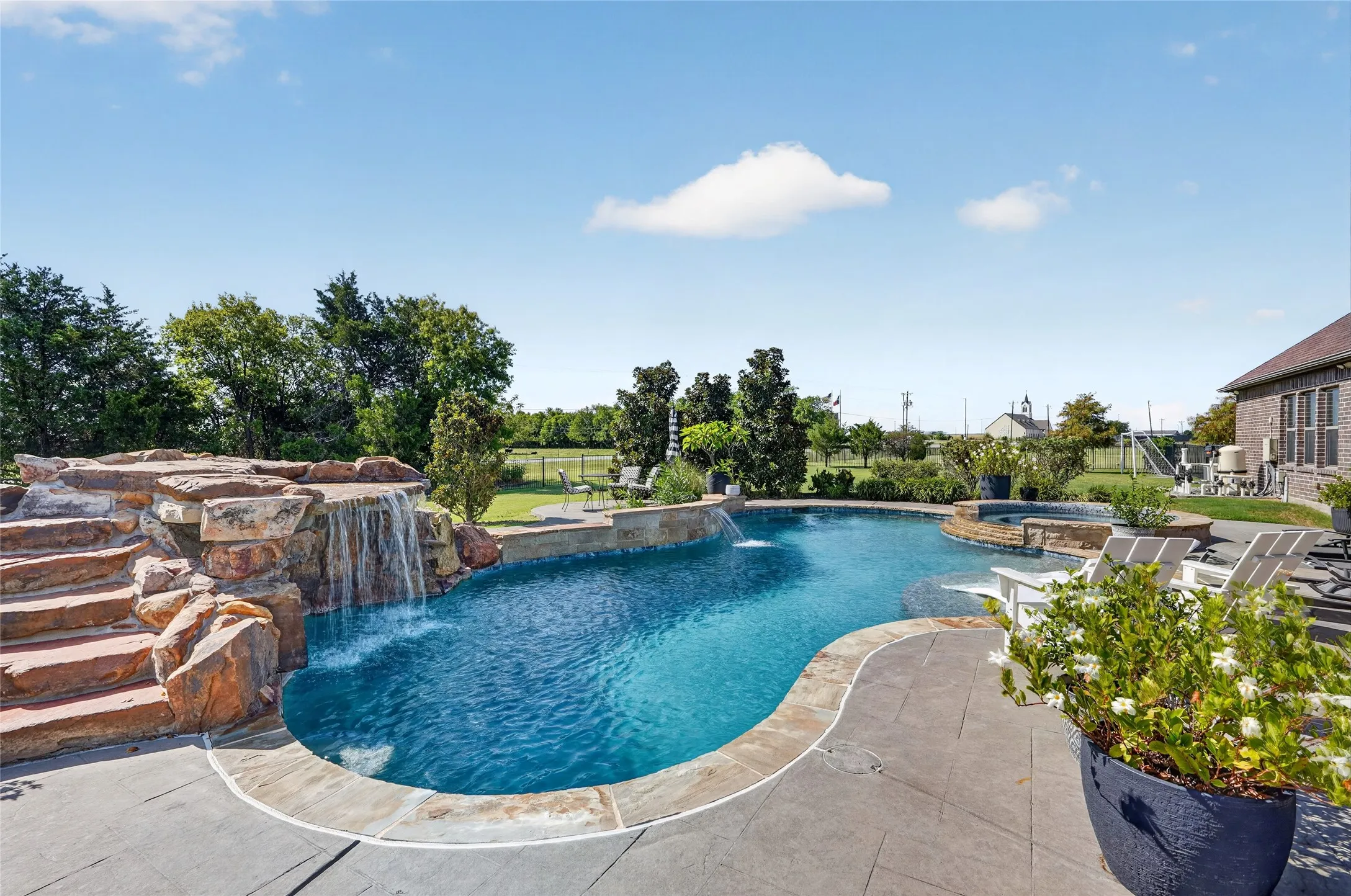 Curved swimming pool with a rock waterfall feature, integrated spa, and surrounding patio