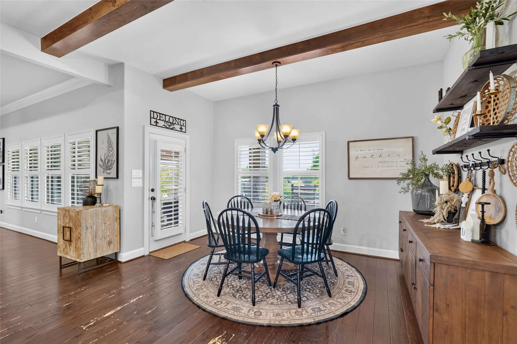 Exposed wood-finish ceiling beams, dark wood-finish flooring, and white plantation shutters on multiple windows