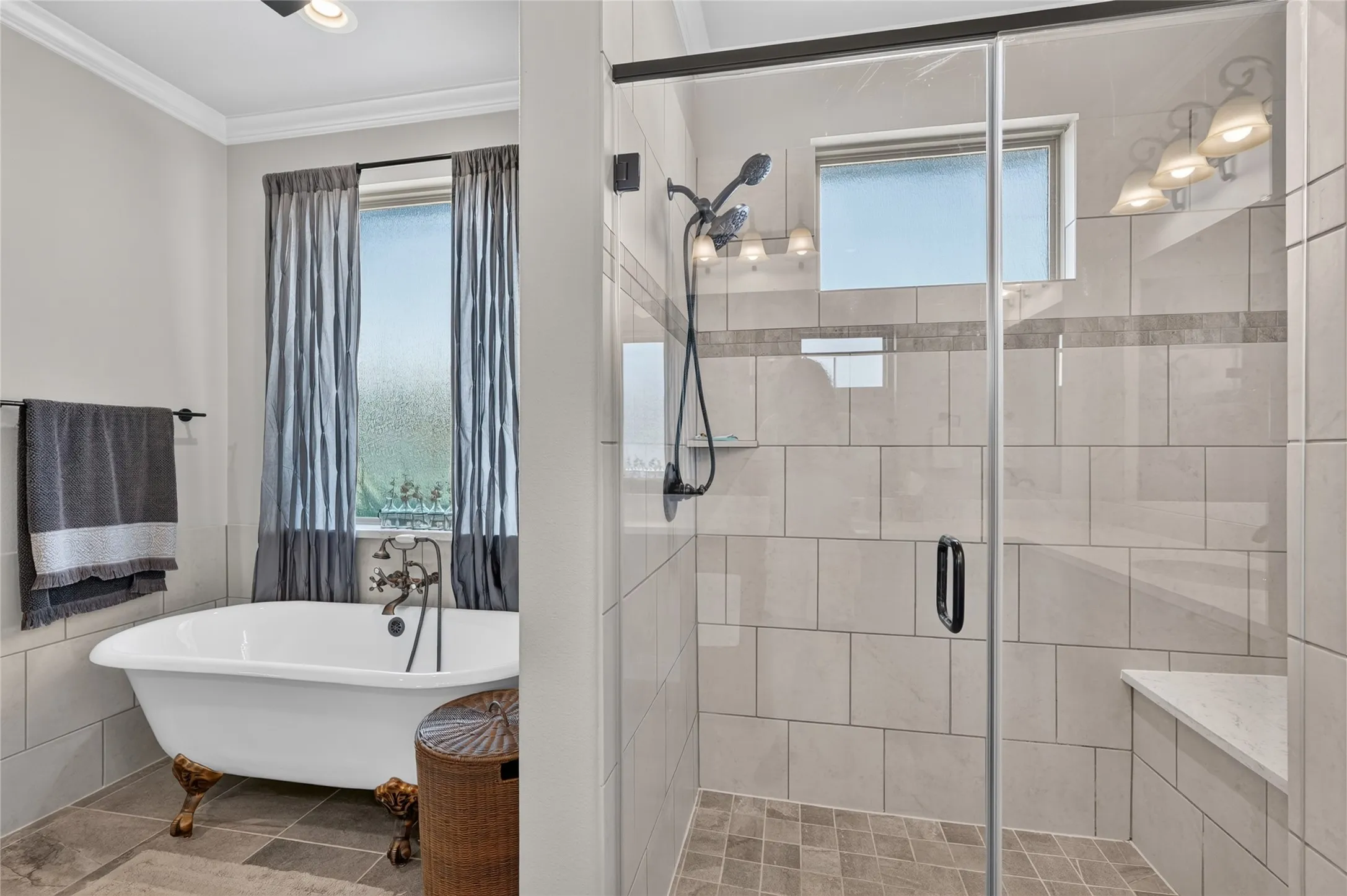 Spa-inspired primary bathroom featuring a freestanding soaking tub with claw feet, walk-in shower with frameless glass enclosure and subway tile surround, dual showerheads, and natural light from operable windows