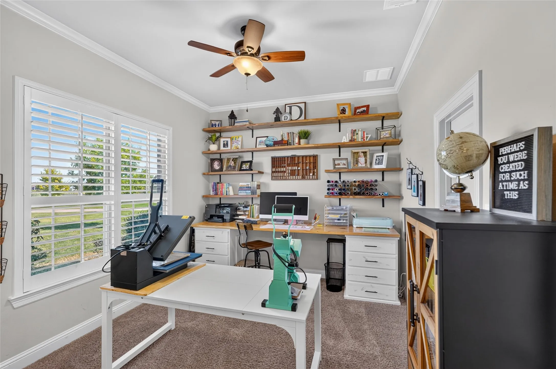 Built-in shelving with wood planks and metal brackets, white window shutters, crown molding, a ceiling fan, and carpeted flooring