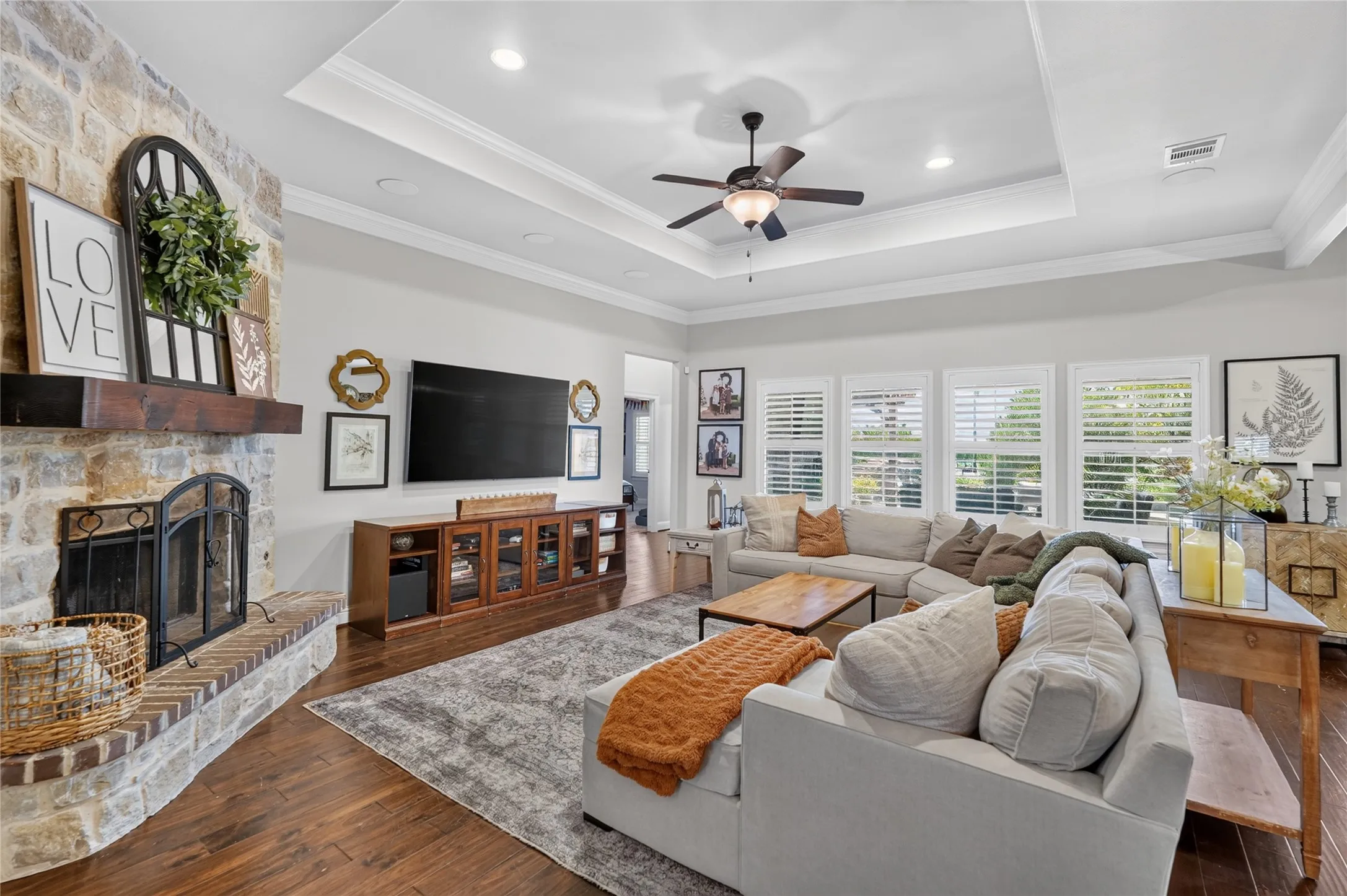 Sophisticated living room featuring a coffered ceiling with recessed lighting and ceiling fan, wood-finish flooring throughout, and a wood-frame media console with built-in cabinetry