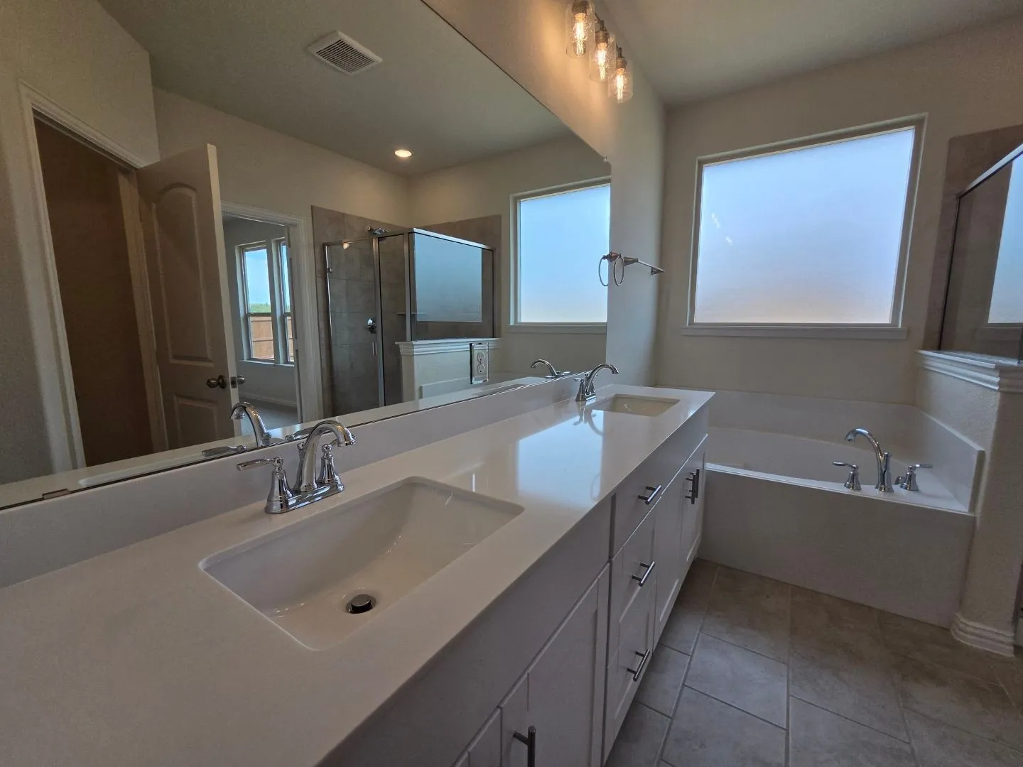 Dual vanity with integrated sinks, chrome fixtures, built-in bathtub, and tiled flooring