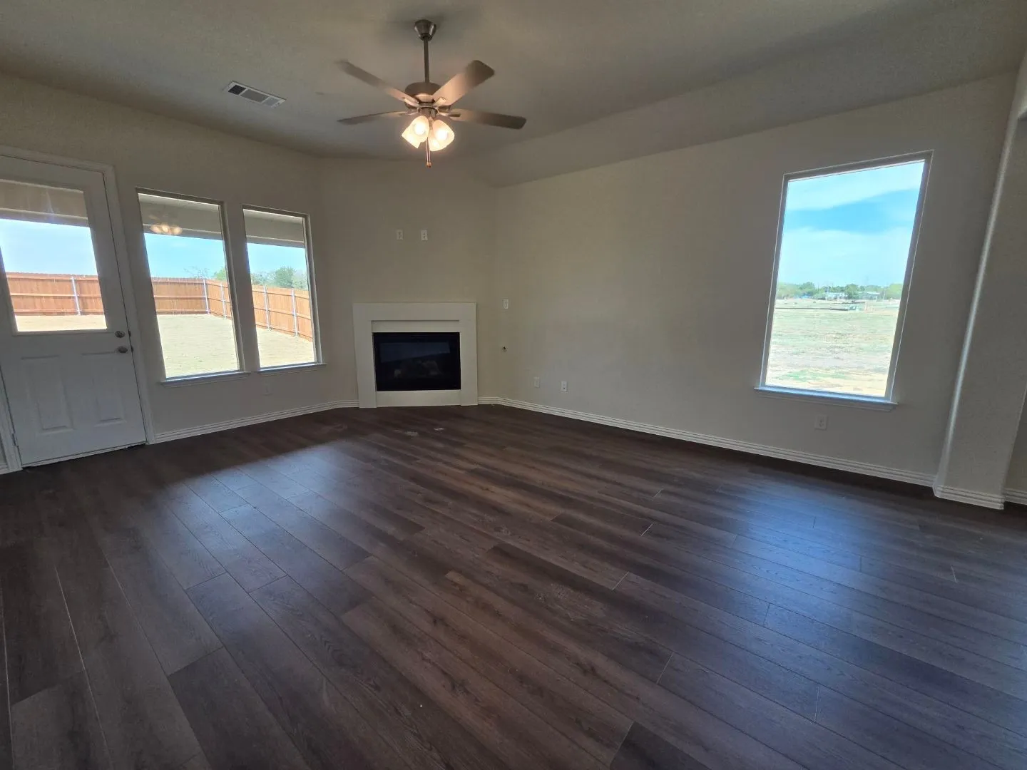 Wood-finish flooring, an electric fireplace with a white mantel, ceiling fan, and multiple windows