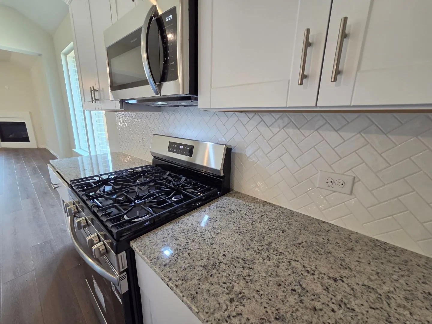 White upper cabinetry with brushed nickel hardware, stainless steel microwave, herringbone tile backsplash, granite countertops, and gas range