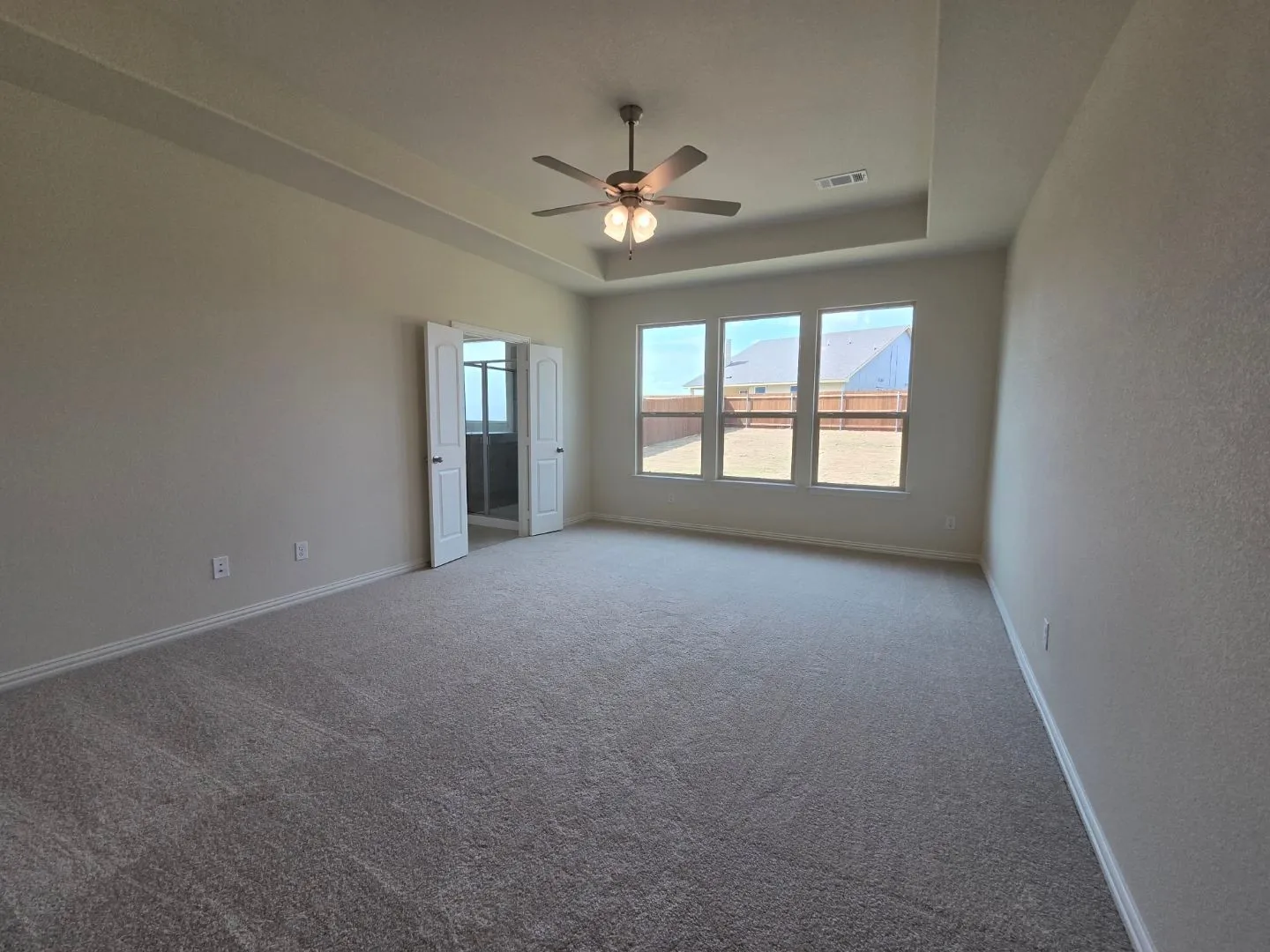 Spacious room featuring neutral carpeting, a tray ceiling, and a ceiling fan with integrated lighting