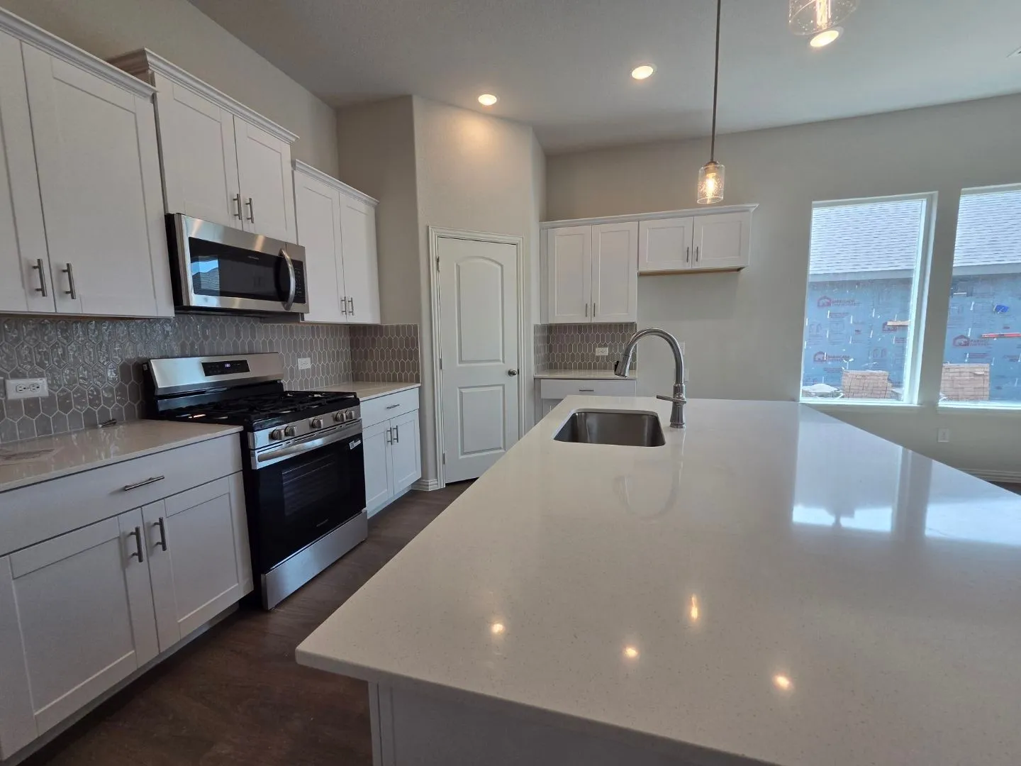 Kitchen featuring white shaker cabinetry, stainless steel appliances, a mosaic tile backsplash, and a large central island with an integrated sink