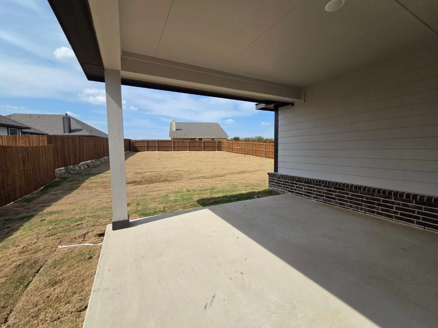 Covered concrete patio with recessed lighting, siding and brick exterior, and a wood privacy fence enclosing the backyard