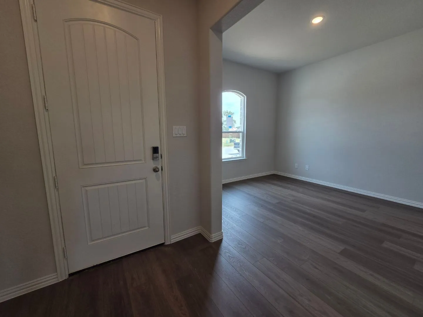 Arched entry door with vertical paneling, wood-finish flooring, and an arched window