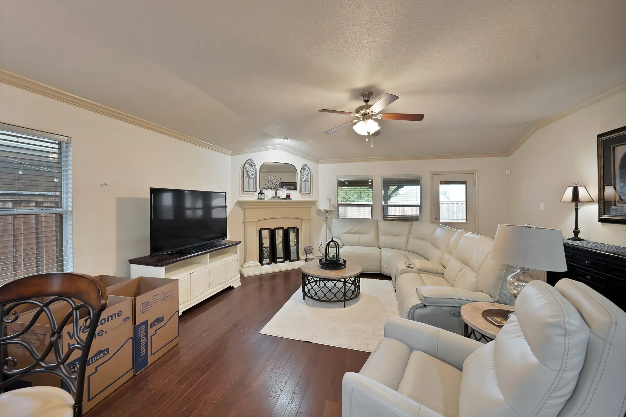 Wood-finish flooring, corner fireplace with mantel, ceiling fan with light fixture, crown molding, and outdoor access