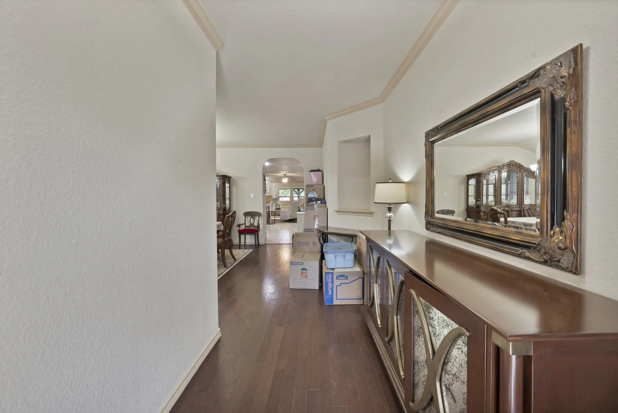 Hardwood flooring extending through the hallway, crown molding, arched entryway, and recessed wall niche