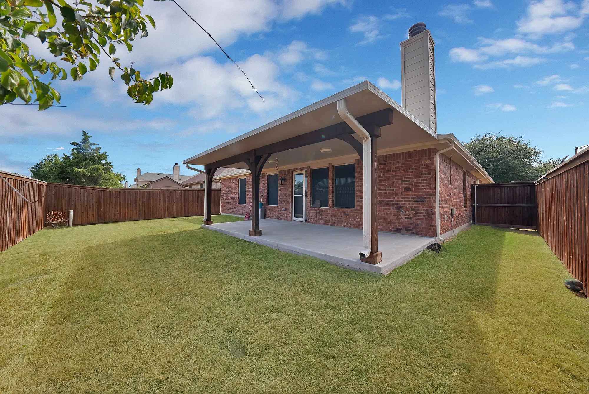 Expansive backyard featuring a manicured lawn, full privacy fencing, and a covered concrete patio with robust support beams