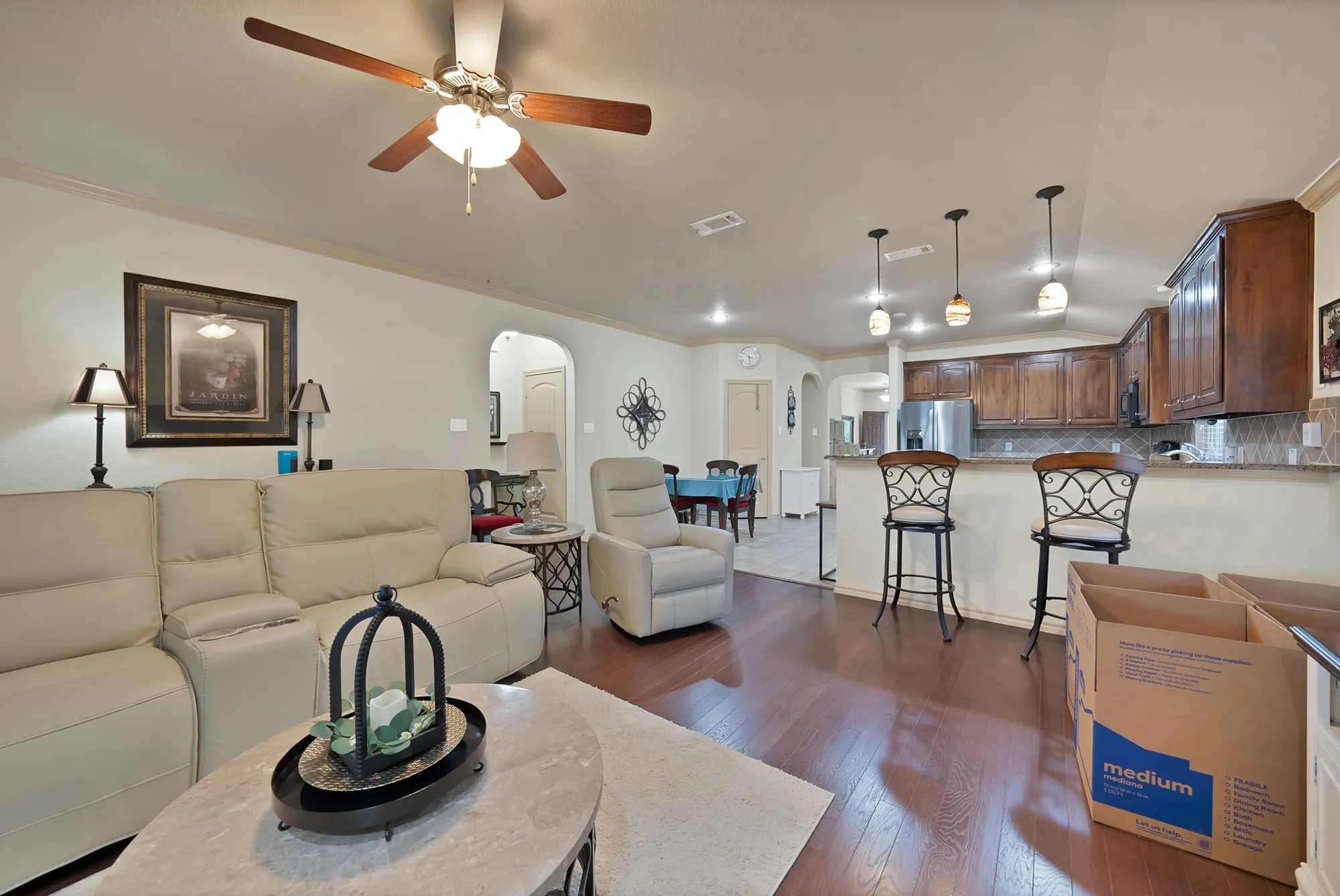 Hardwood-style flooring, tray ceiling with ceiling fan, recessed lighting, kitchen with wood-finish cabinetry, and a breakfast bar