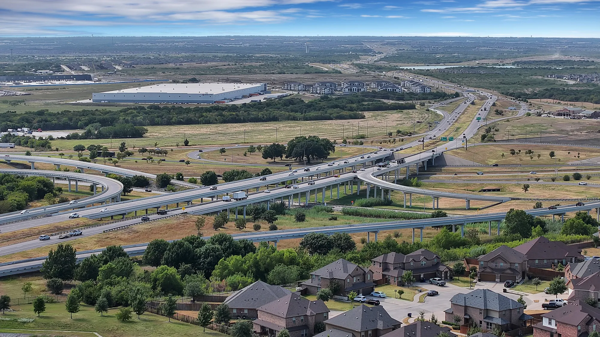 Aerial perspective showcasing residential development, extensive roadway infrastructure, and distant commercial buildings