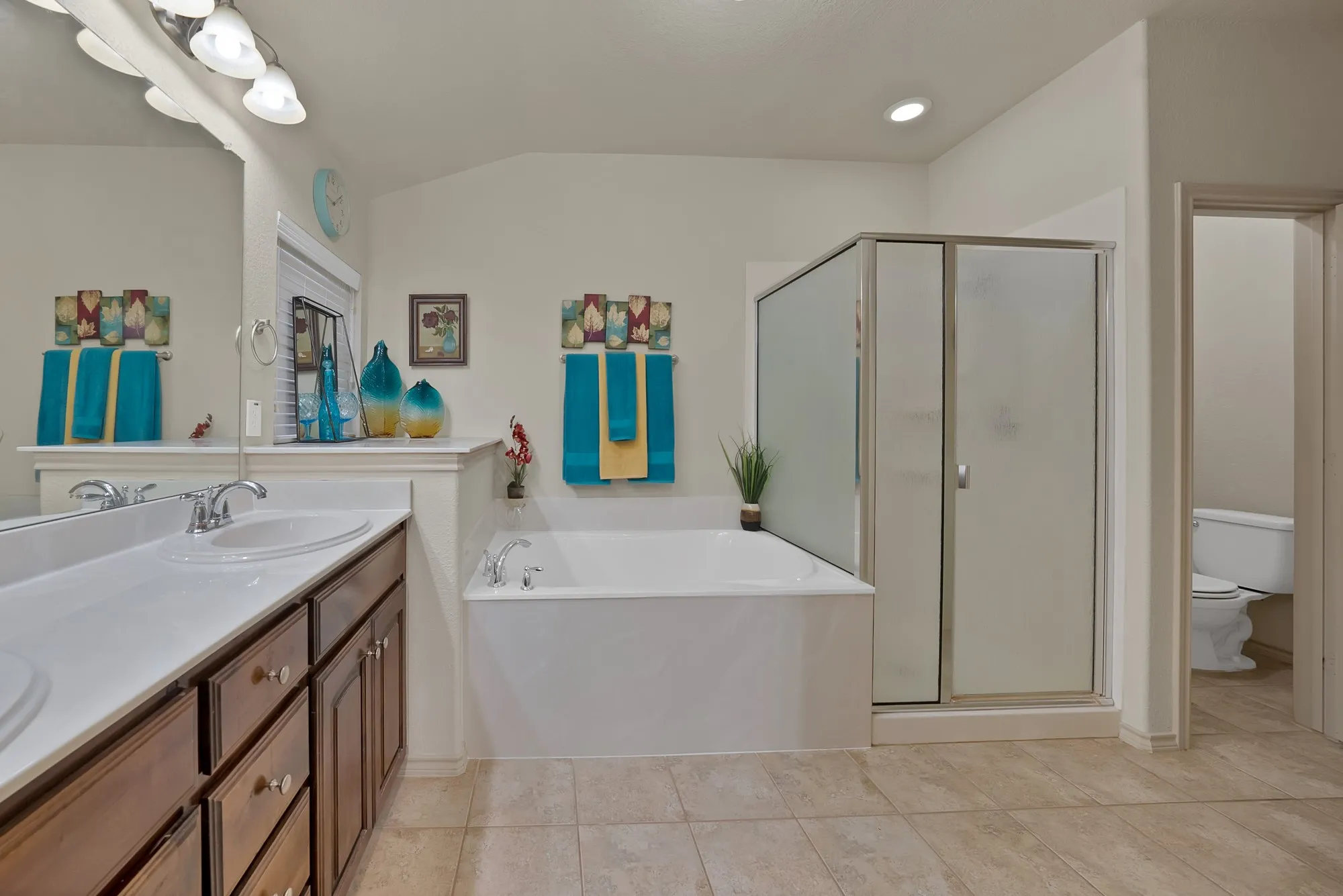 Dual vanity with integrated sinks, wood-finish cabinetry, built-in soaking tub, and enclosed shower with frosted glass