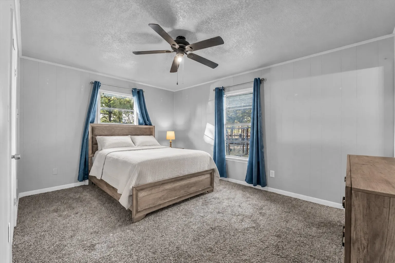 Carpeted flooring, two windows with trim, ceiling fan light fixture, and vertical paneling on walls