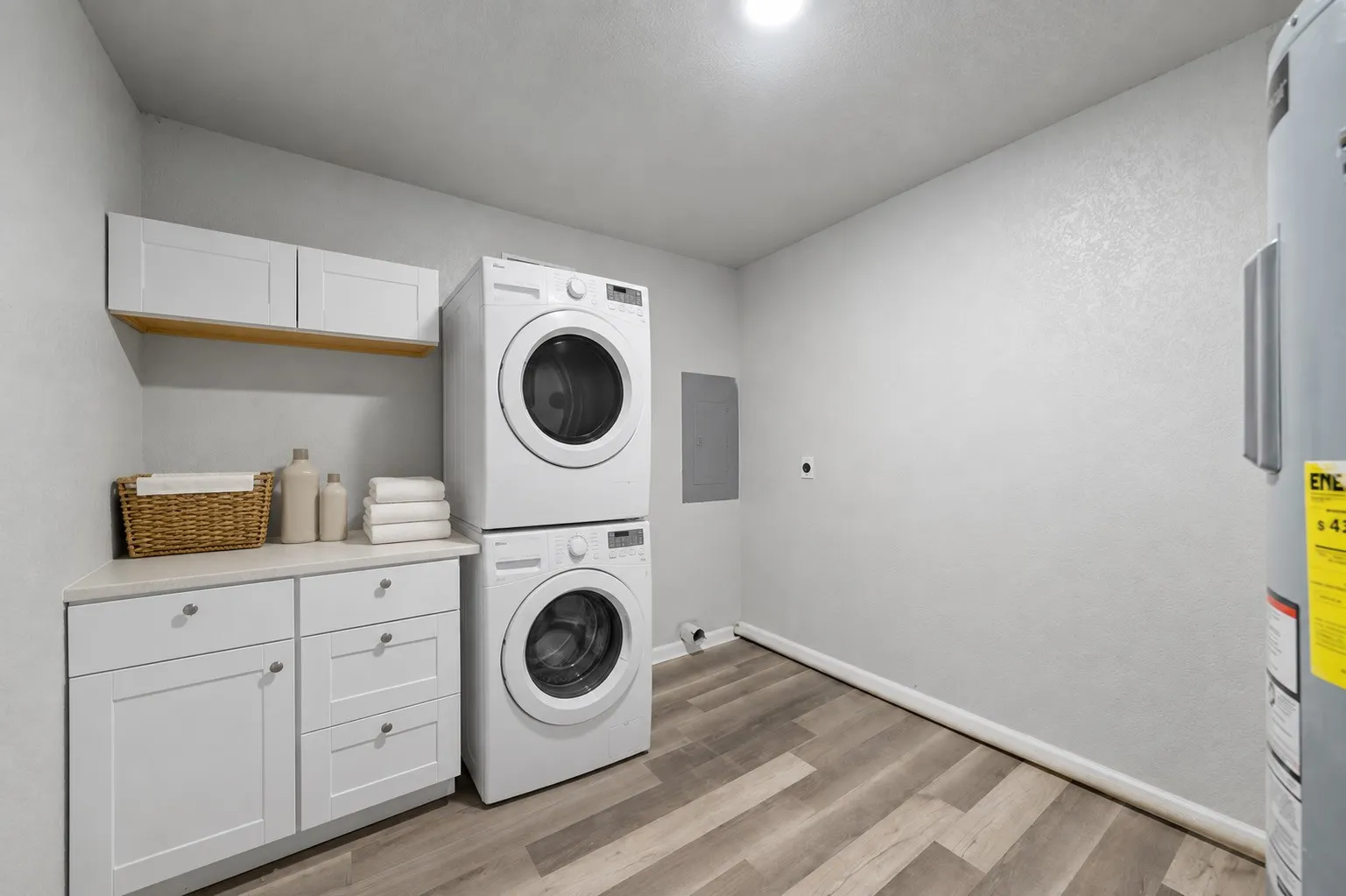 Dedicated utility space featuring wood-finish flooring, white cabinetry with a light-toned countertop, and overhead storage