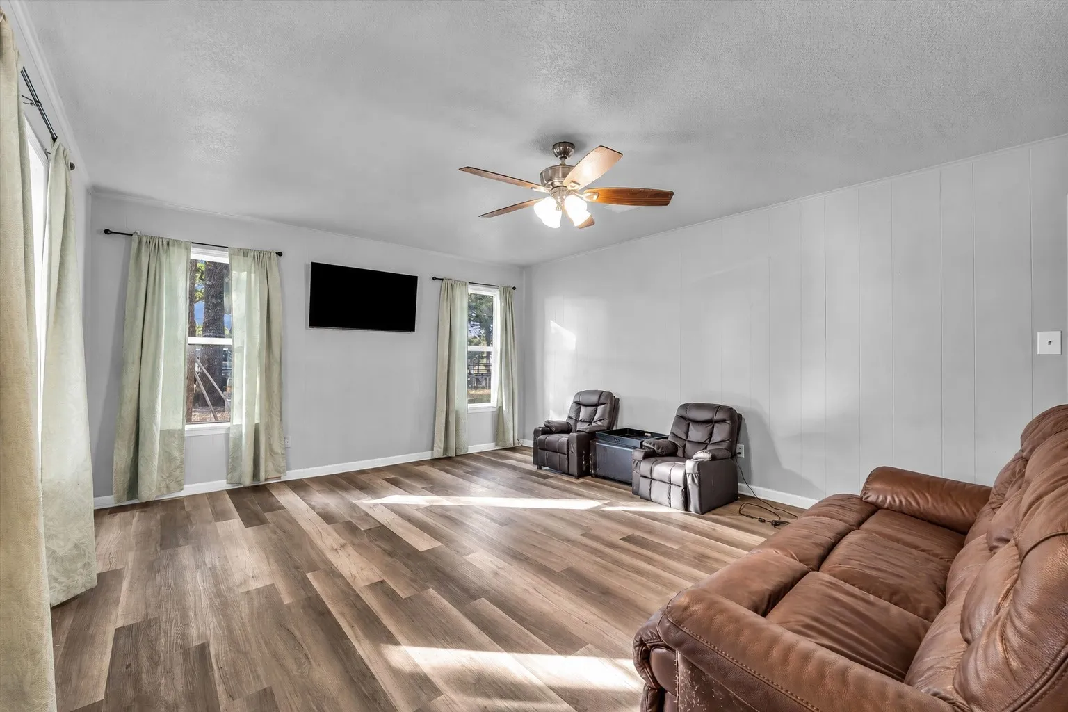 Wood-finish flooring throughout, multiple windows with natural light, and a ceiling fan with integrated lighting