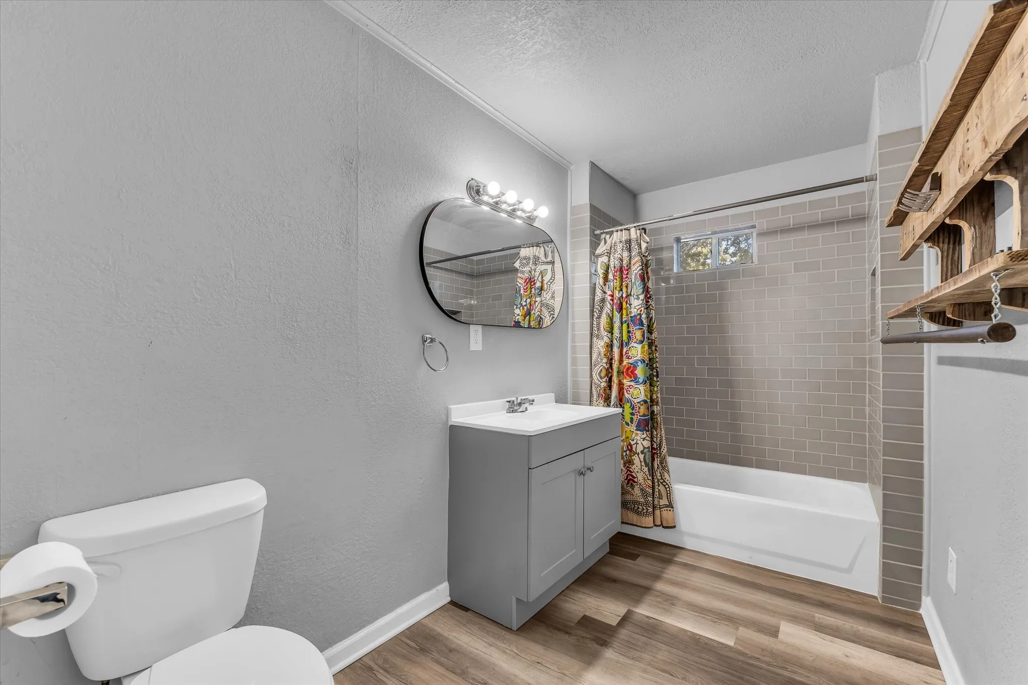Wood-finish flooring, single vanity with integrated sink, modern lighting fixture, subway tile bath surround, and a white bathtub