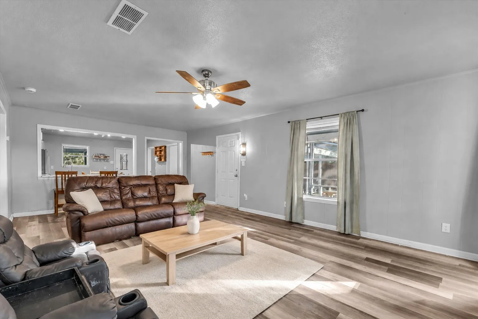 Spacious living area featuring wood-finish flooring, a ceiling fan, and a large window