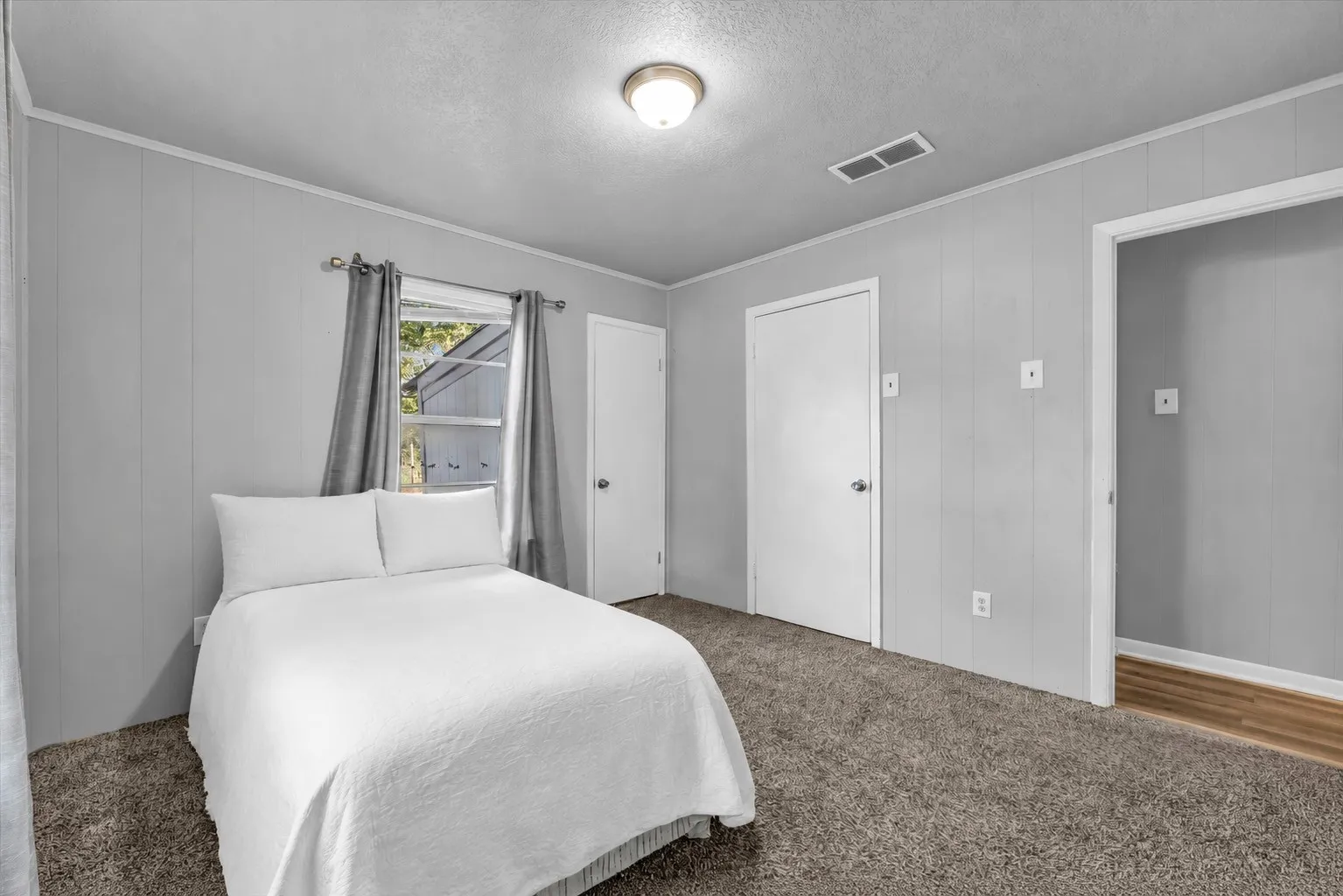 Wall-to-wall carpeting in a neutral tone, vertical paneling on walls, a window with natural light, a flush-mount ceiling light fixture, and a white interior door