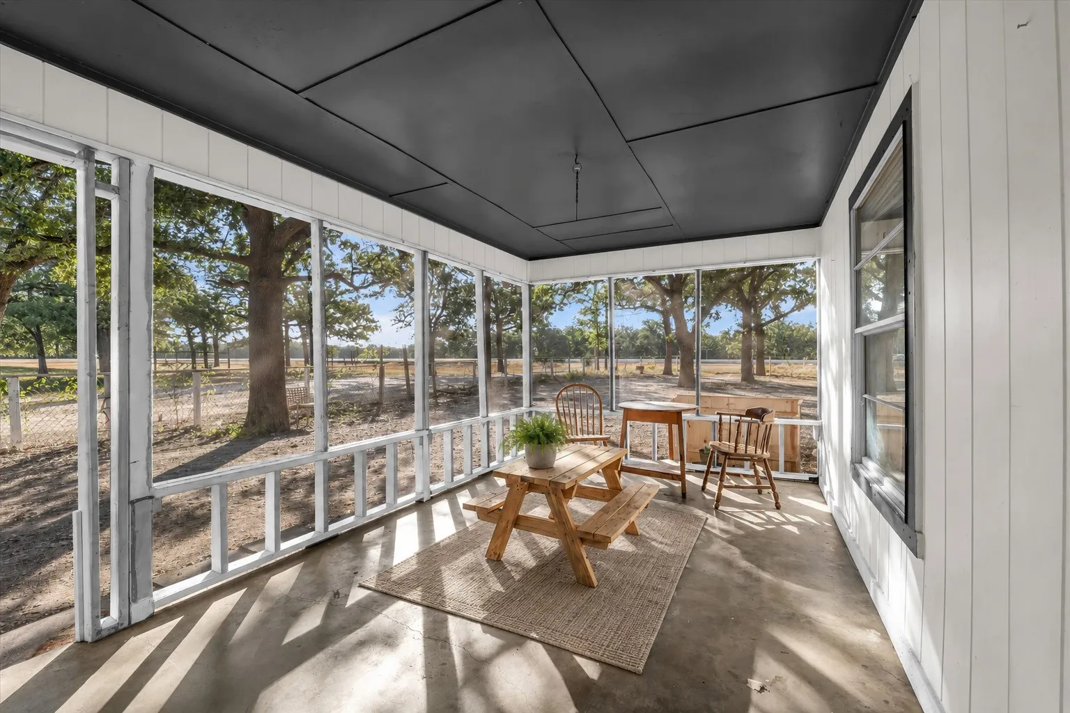 Screened porch with concrete flooring, vertical plank wall paneling, a dark flat panel ceiling, and exterior window