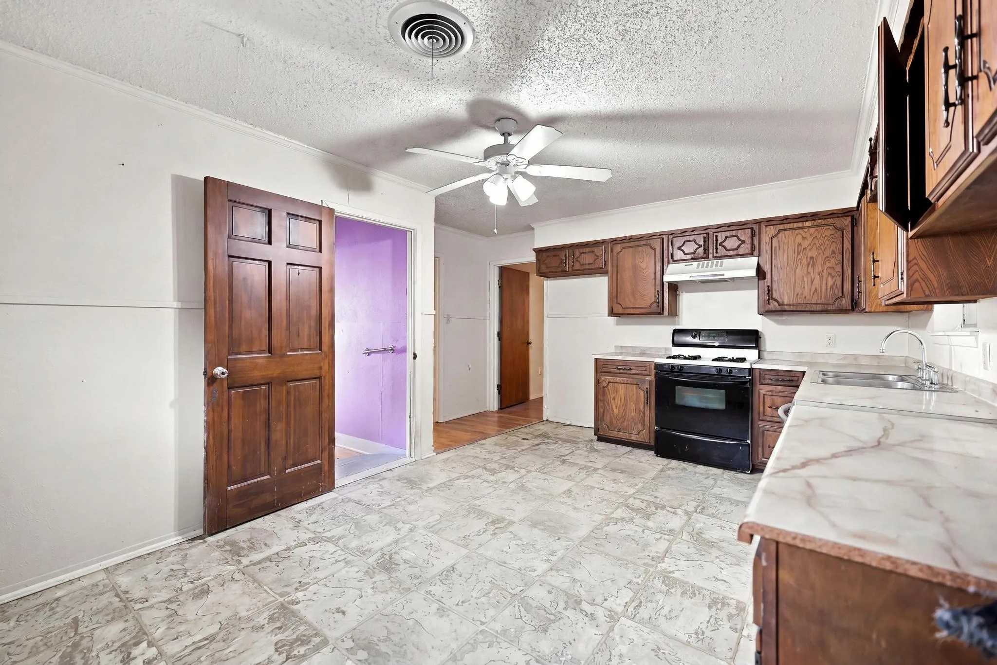 Kitchen featuring a ceiling fan, black range, stainless steel sink, wood cabinetry, and a light-toned countertop