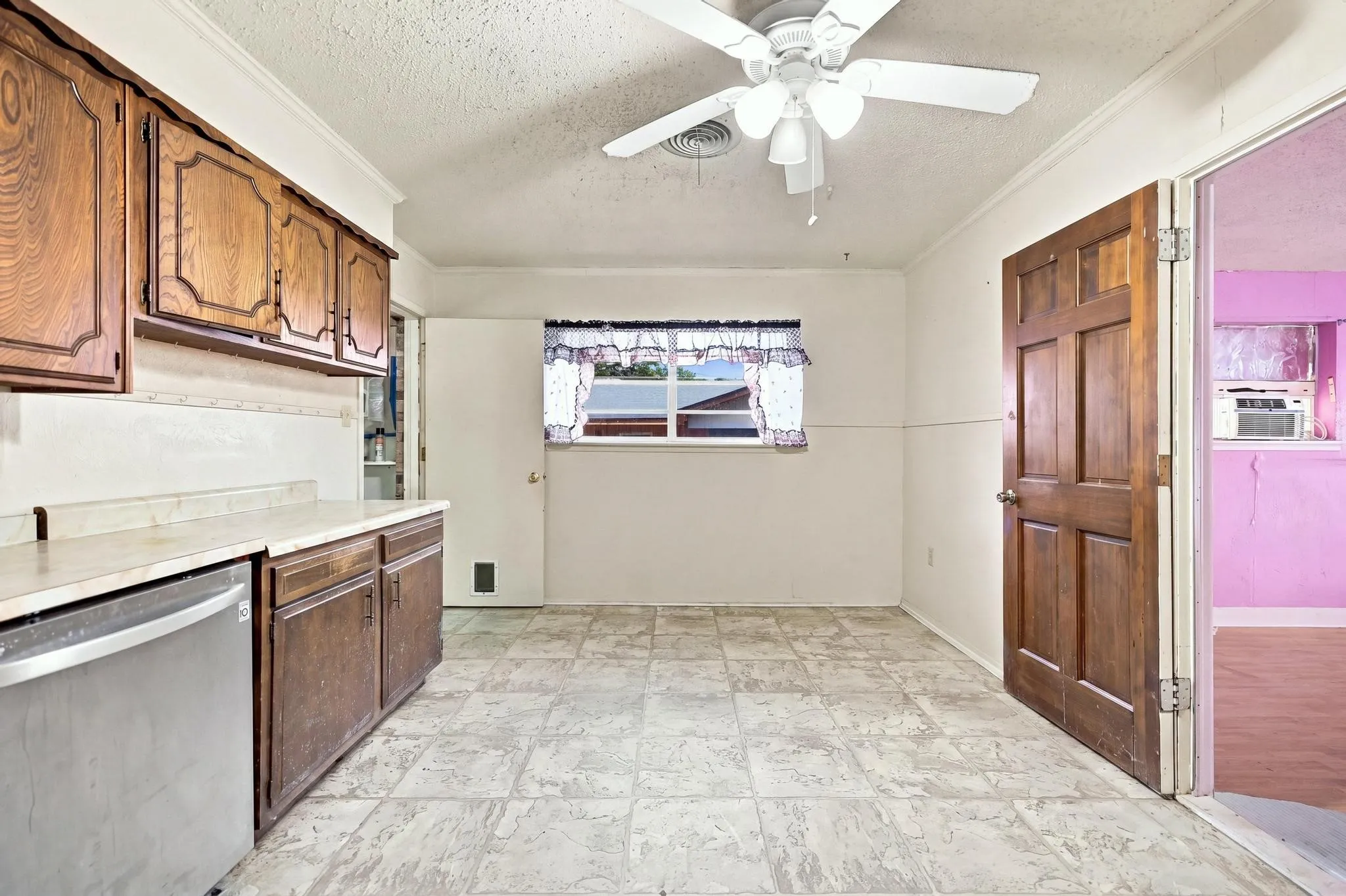 Kitchen featuring wood cabinetry, light-toned countertops, a stainless steel dishwasher, a ceiling fan, and tiled flooring
