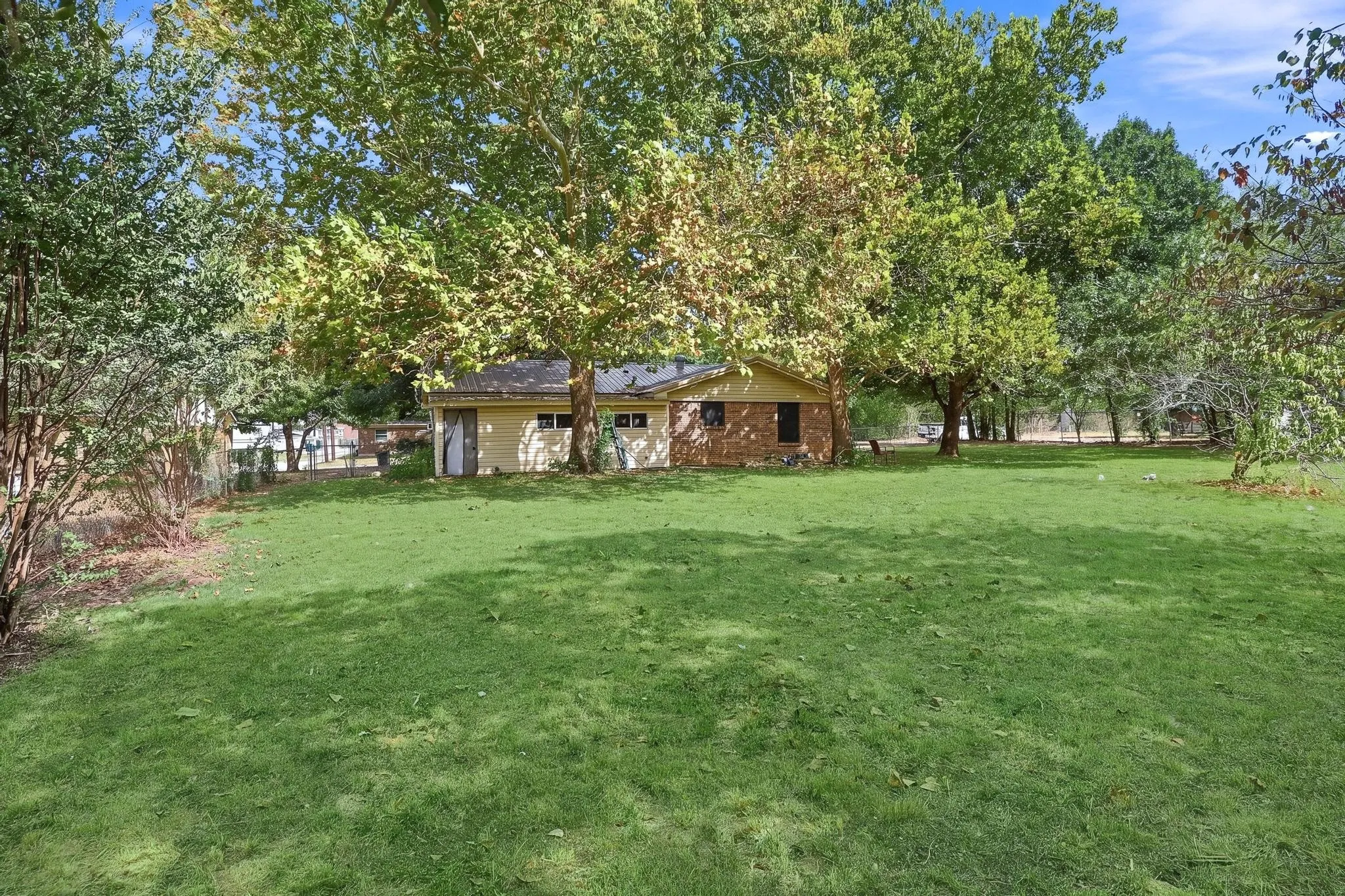 Expansive green lawn with mature trees and a detached structure featuring a brick and siding exterior
