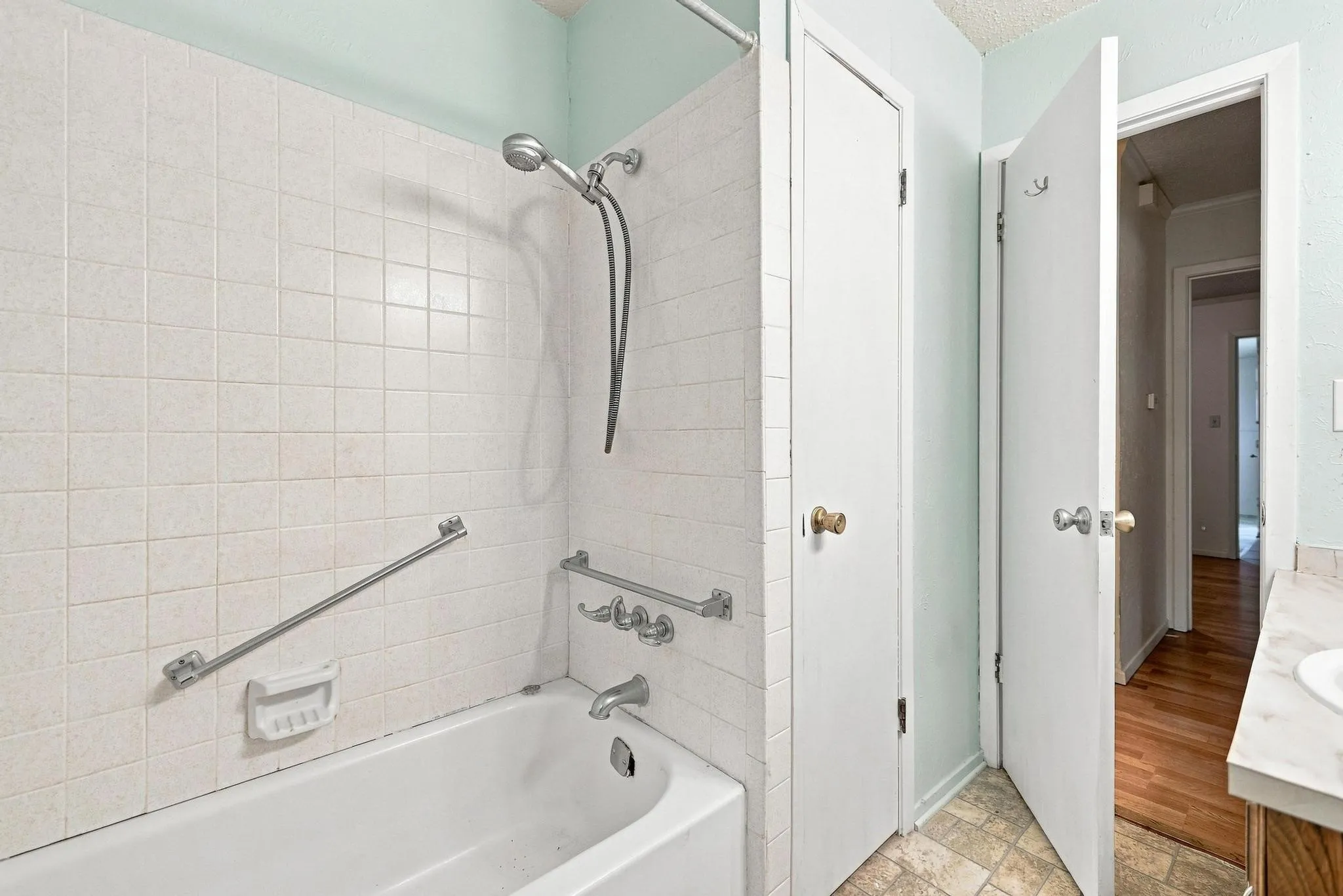 Bathtub with white tile surround, grab bars, and a handheld showerhead