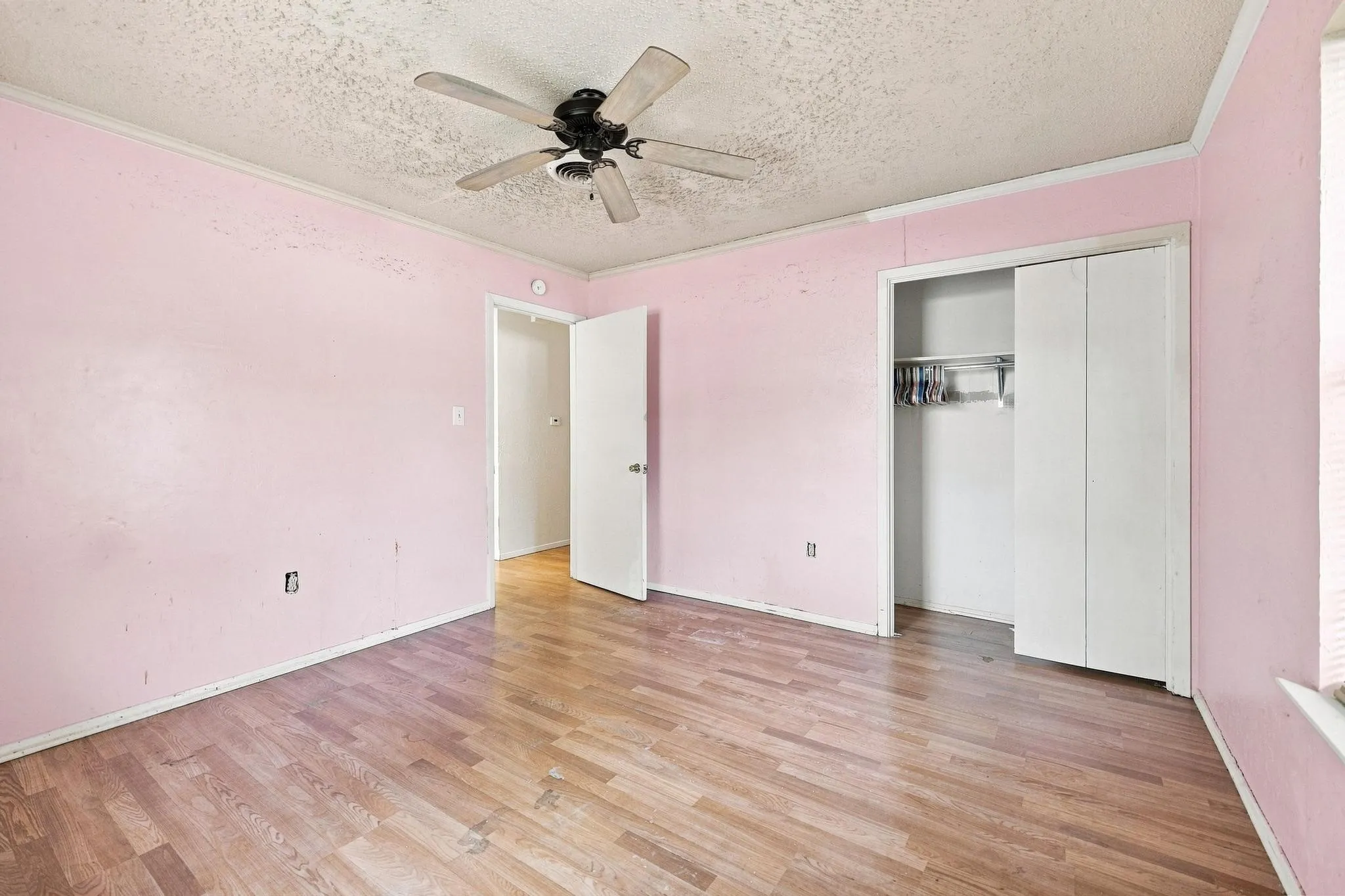 Wood-finish flooring with a ceiling fan light fixture and a built-in closet with bi-fold doors