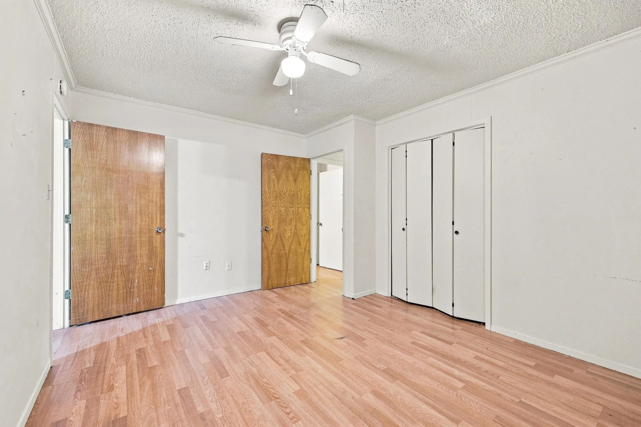 Wood-finish flooring, ceiling fan with integrated lighting, wood-paneled doors, and bi-fold closet doors